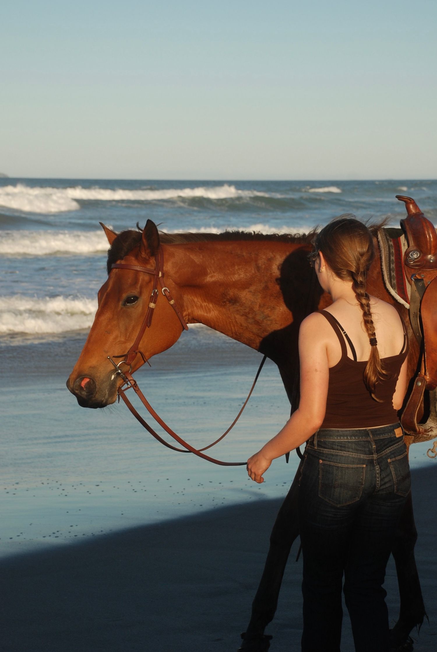 Candid shot of a woman standing beside her horse near the ocean waves