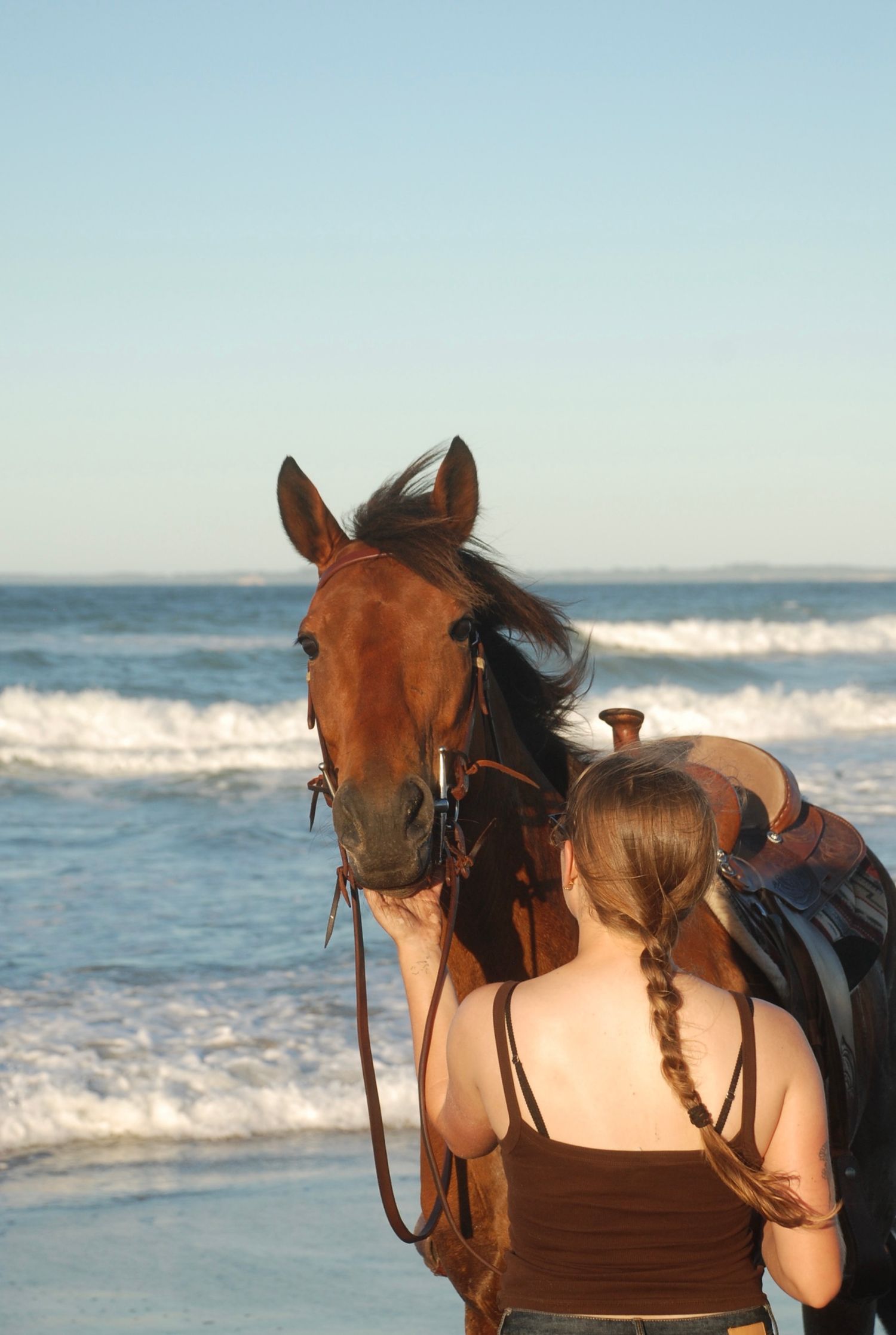 Woman with her back to the camera, horse’s face over her shoulder looking at the lens
