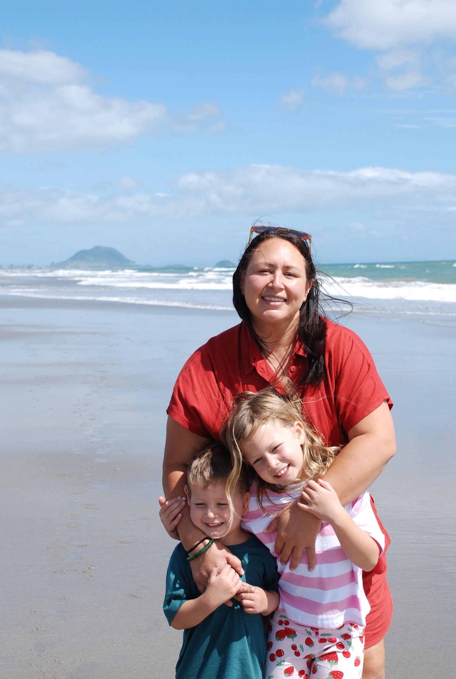 Mum hugging her son and daughter while they smile at the camera.