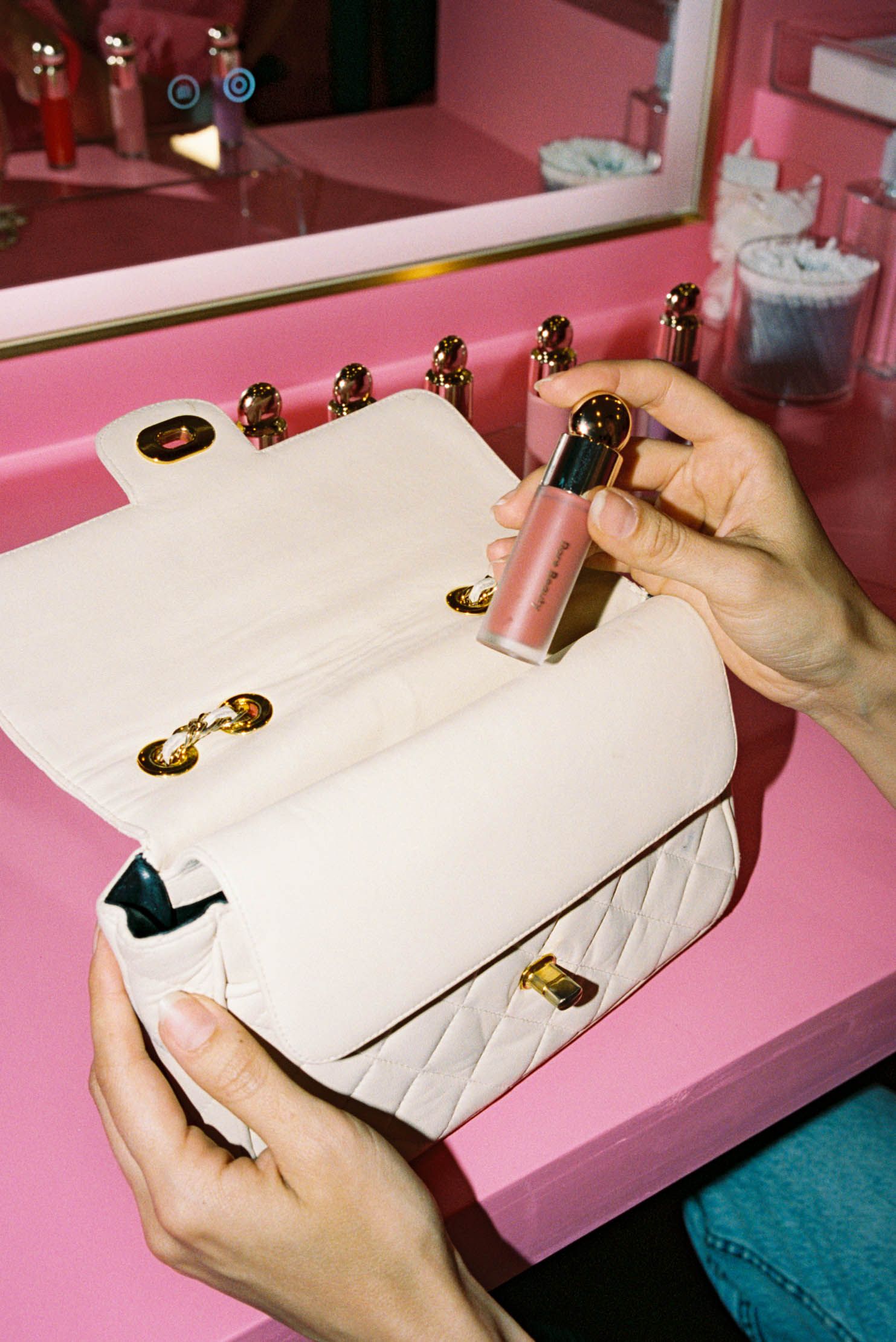 A sequence showing hands attaching decorative gold hardware onto a white leather purse or handbag on a pink surface.