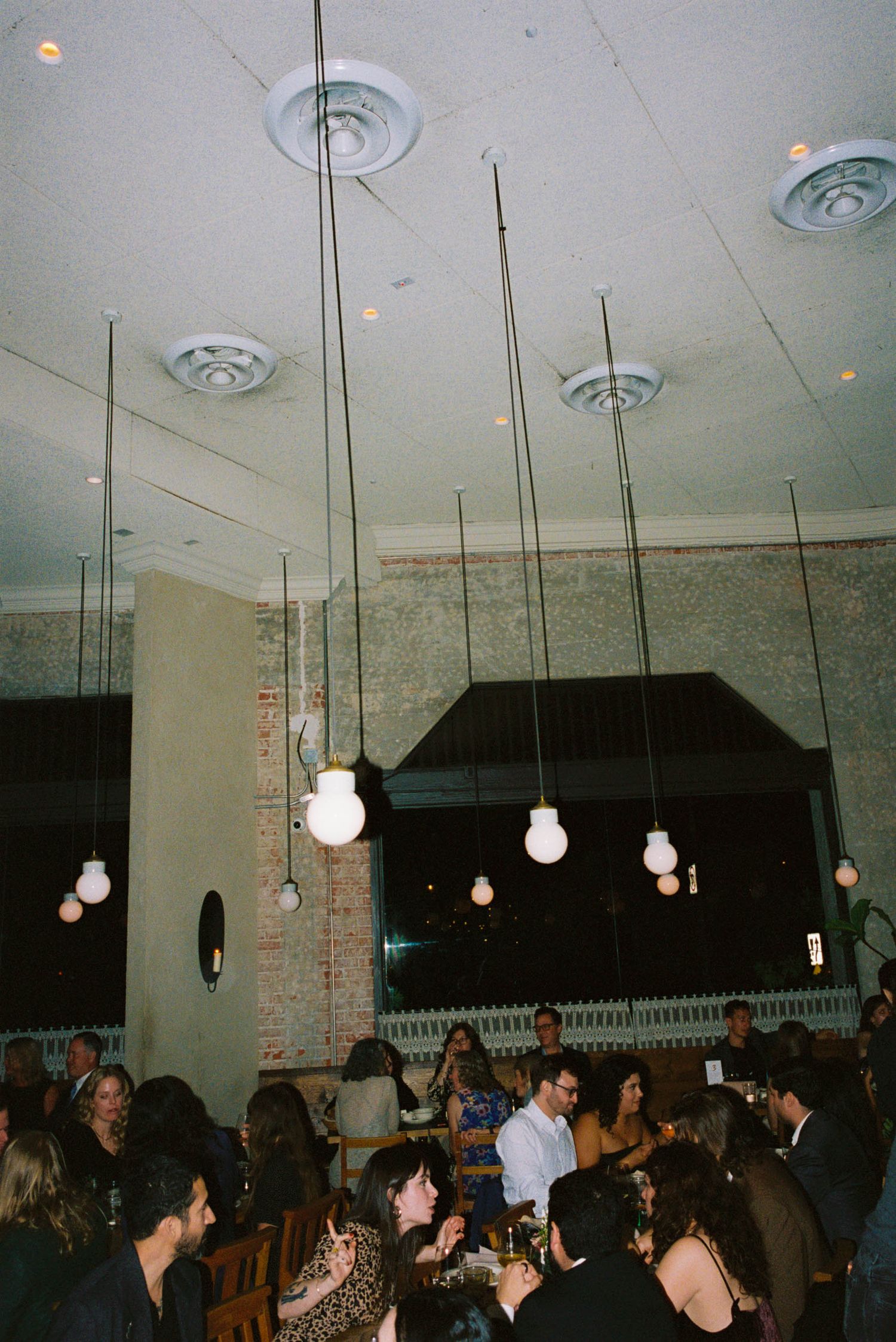Crowded restaurant interior with hanging pendant lights and exposed brick walls.