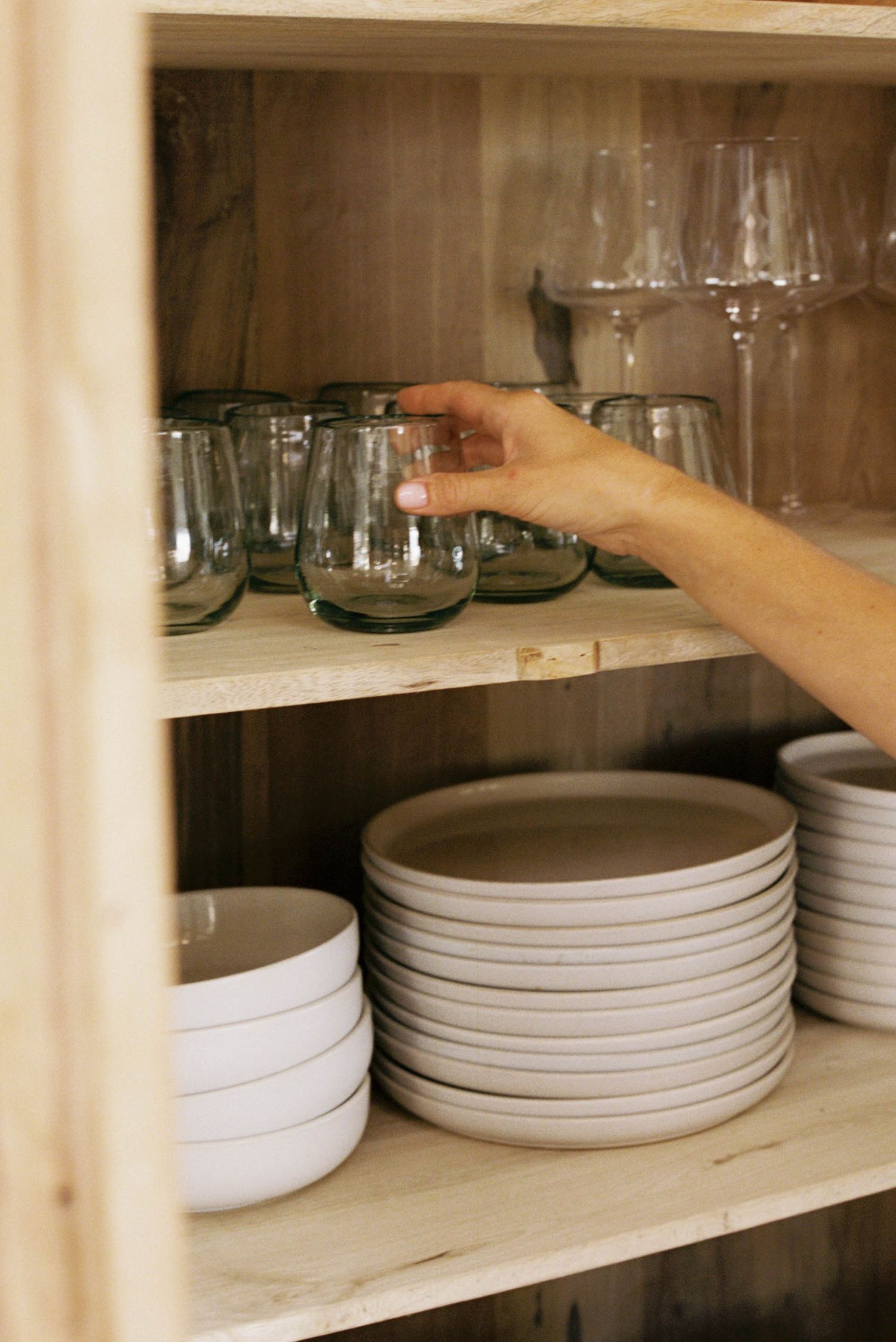 White ceramic plates and glass drinkware arranged neatly on wooden shelves in a kitchen cabinet.