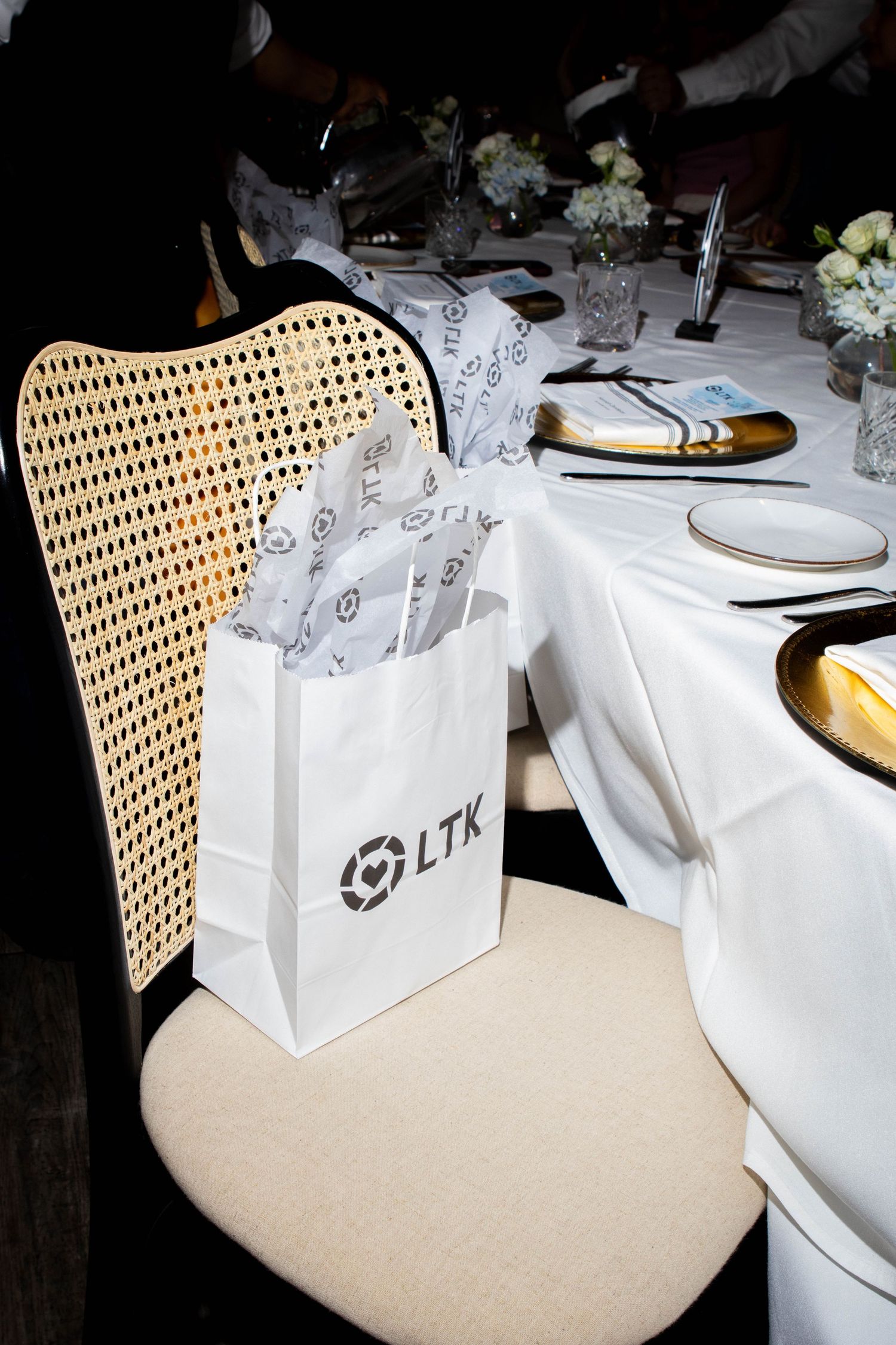 White shopping bags with LTK logo arranged on dining table with cane-backed chairs.