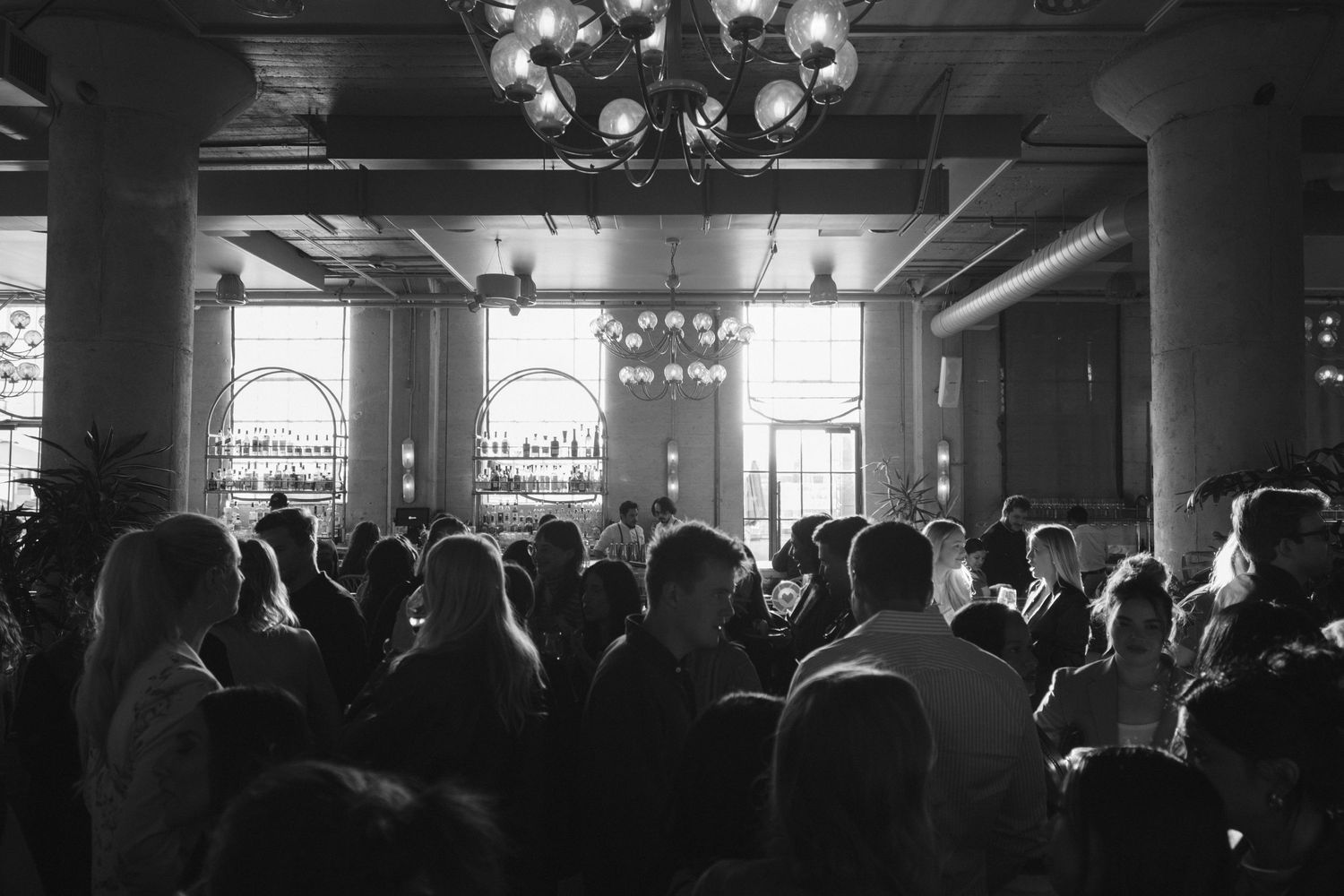 A dimly lit nightclub or concert venue filled with silhouettes of people standing in a crowd.