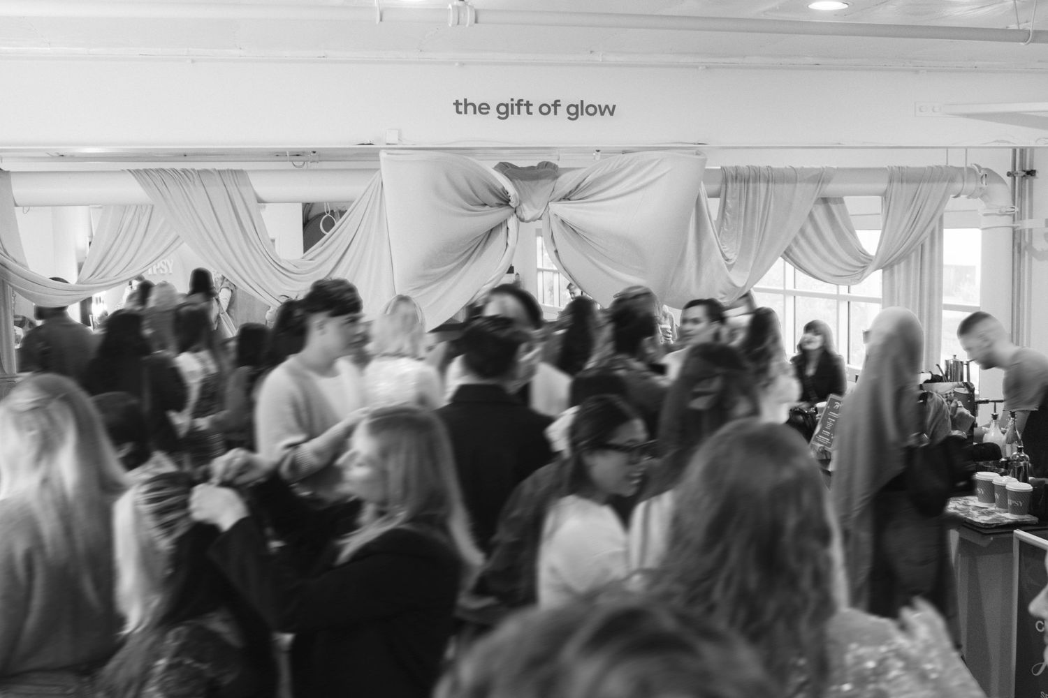 Crowded indoor event space with people mingling under white tent structures.