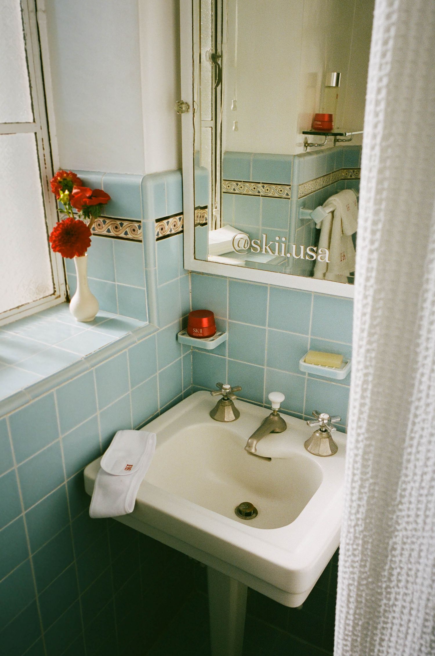 Vintage bathroom with blue tile walls, white sink, and floral shower curtain.