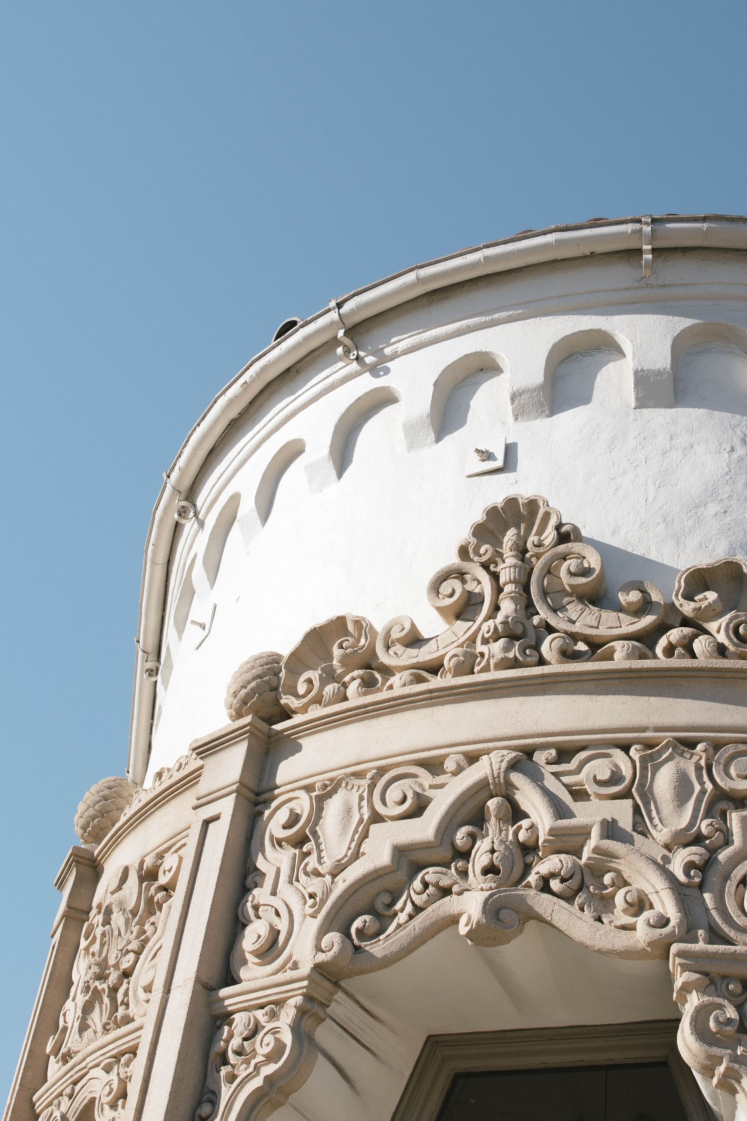 Ornate white architectural detail with decorative scrollwork and arches against a blue sky on a historic building exterior.