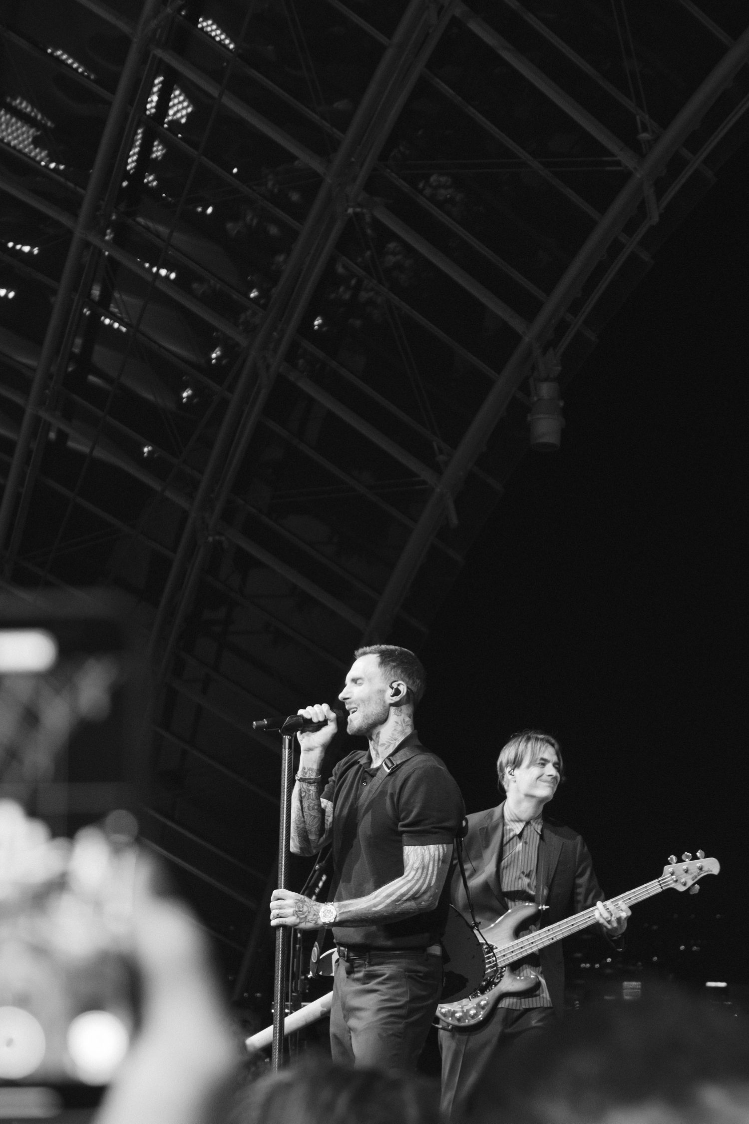 Black and white photo of a tattooed male singer performing on stage with a bassist behind him at an outdoor concert.