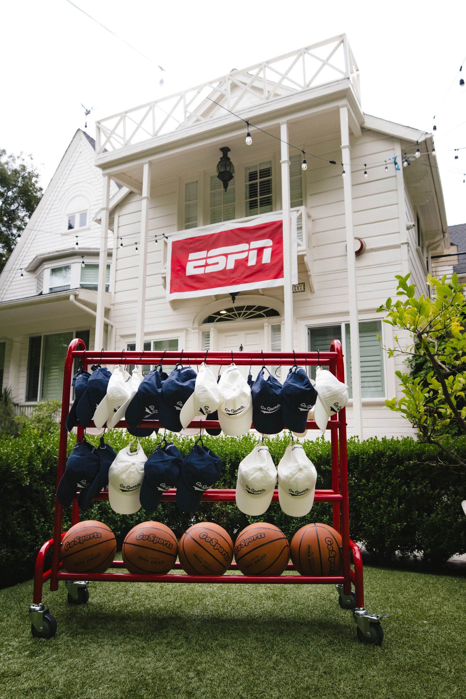 A row of white sports caps displayed on a red ESPN-branded bench with footballs lined up on the grass.