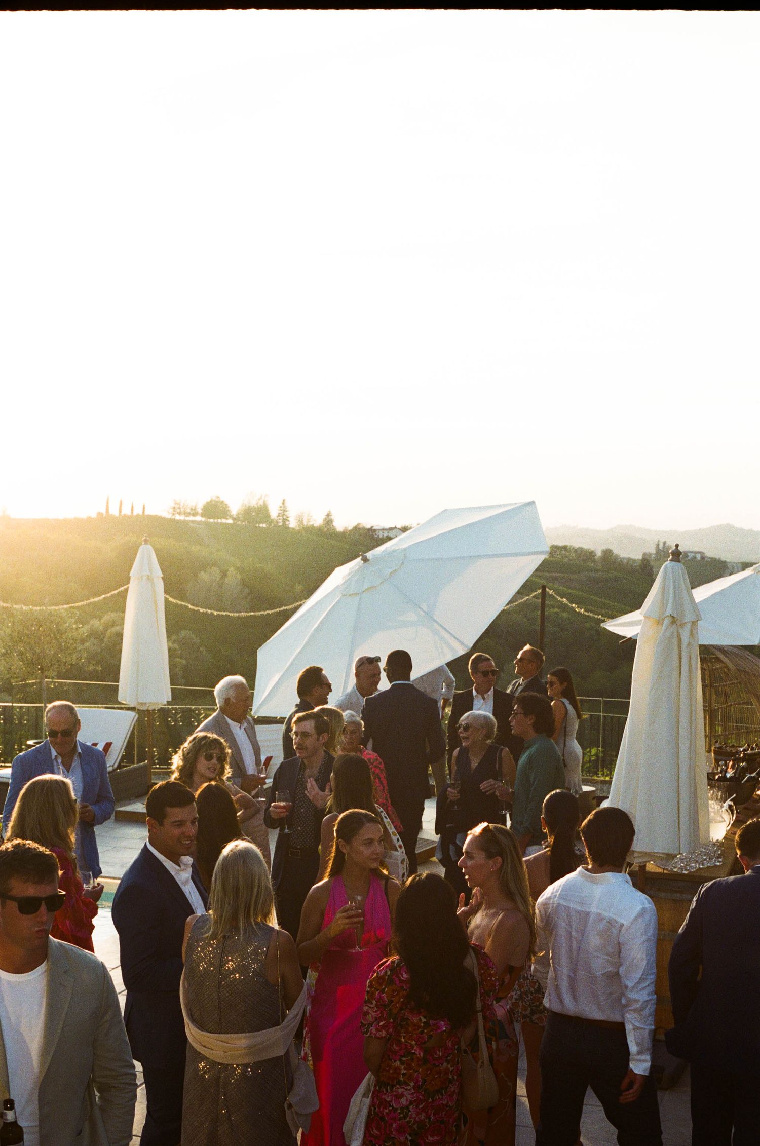 Wedding guests mingle at an outdoor reception during golden hour with white canopy tents and scenic views.