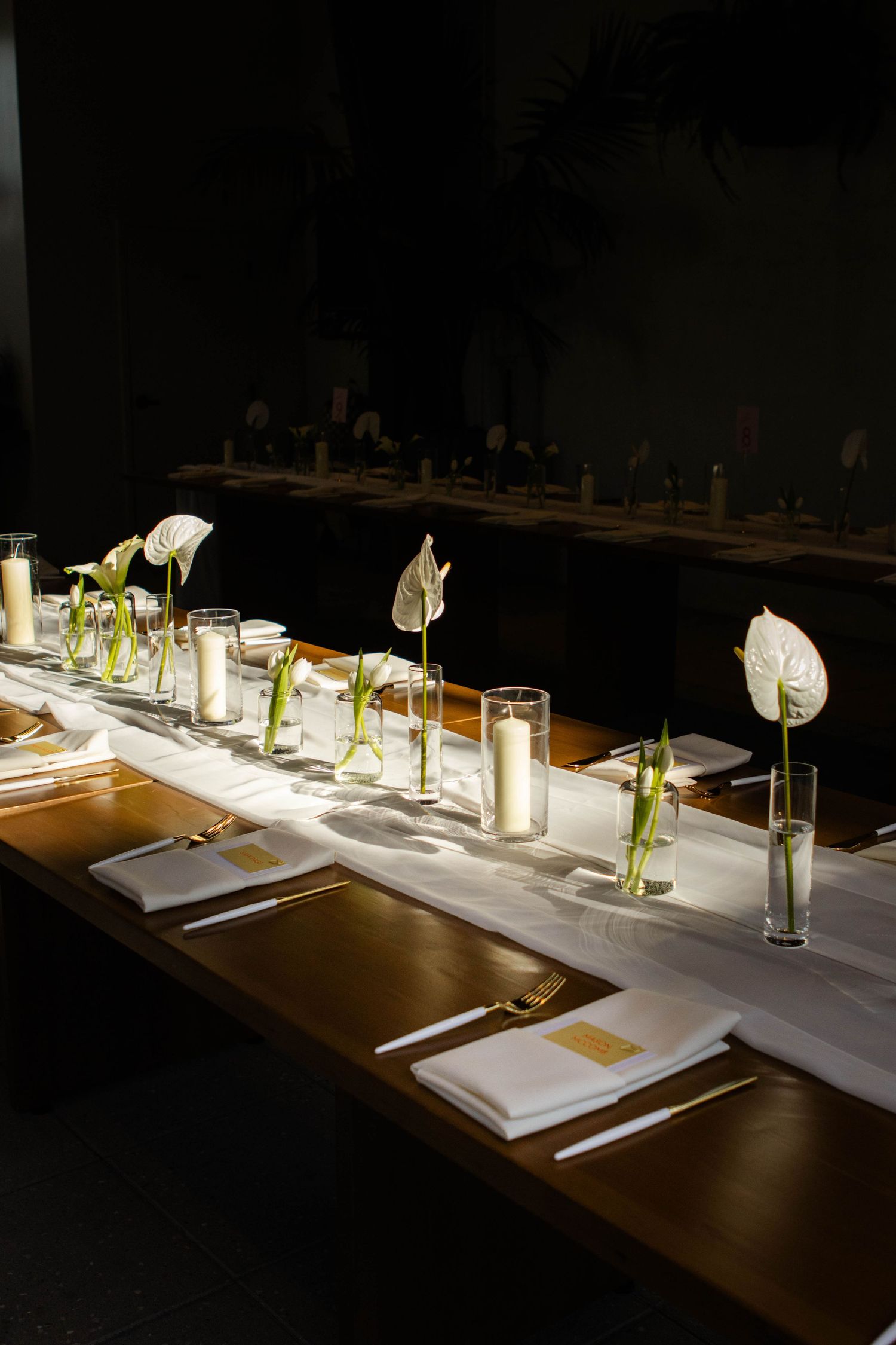 Elegant table settings in a dimly lit restaurant with white peace lily flowers and glowing candles creating ambiance.