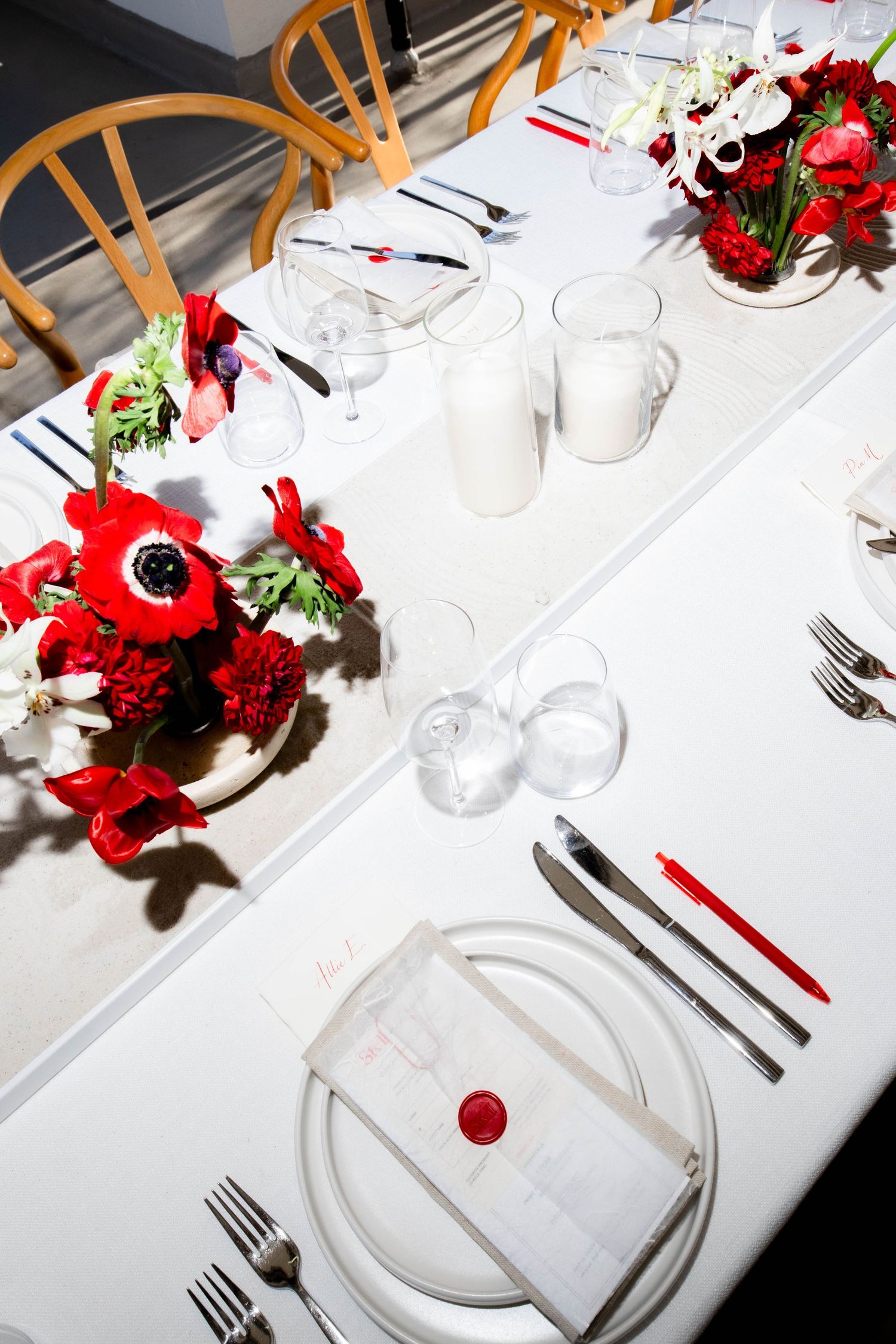 Formal table setting with white linens, red flowers and place settings.