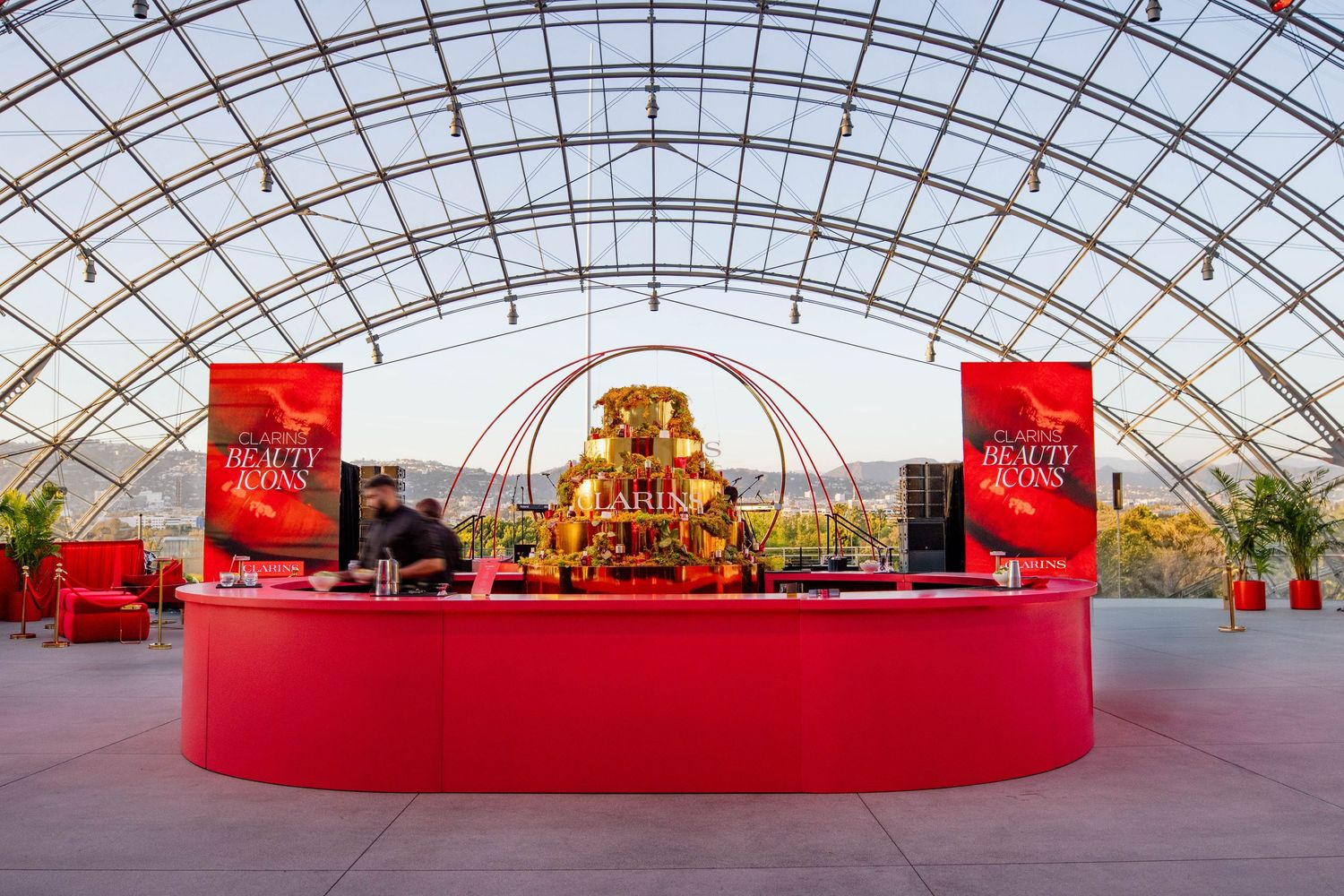 Spacious event venue with arched glass roof and red stage platform featuring elegant display arrangements.