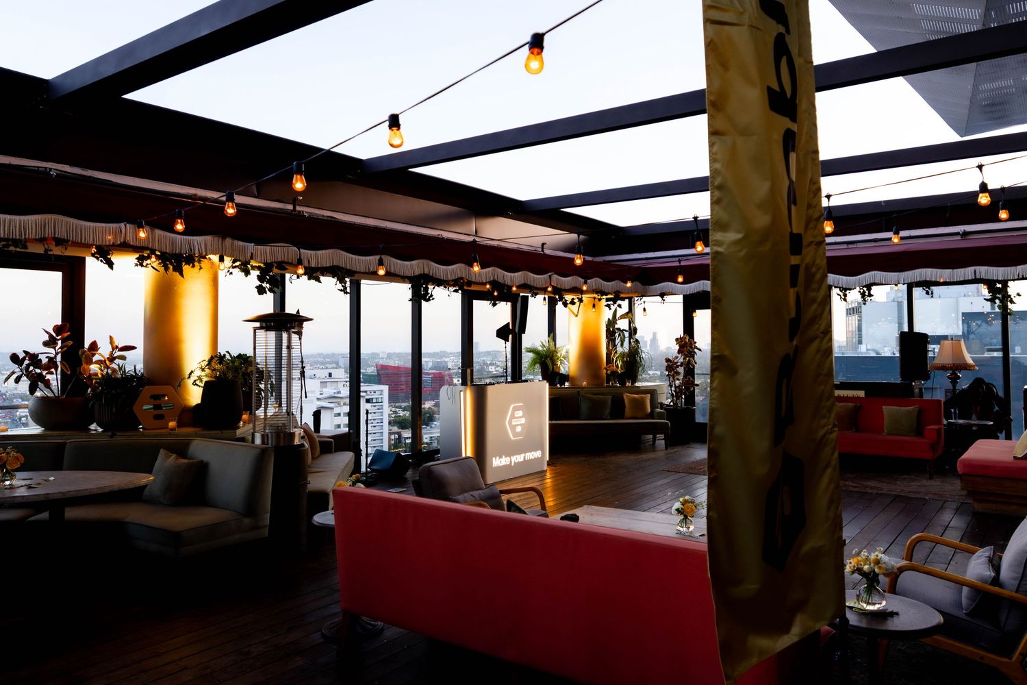 Stylish rooftop bar with string lights, red sofas, and panoramic city views at dusk.