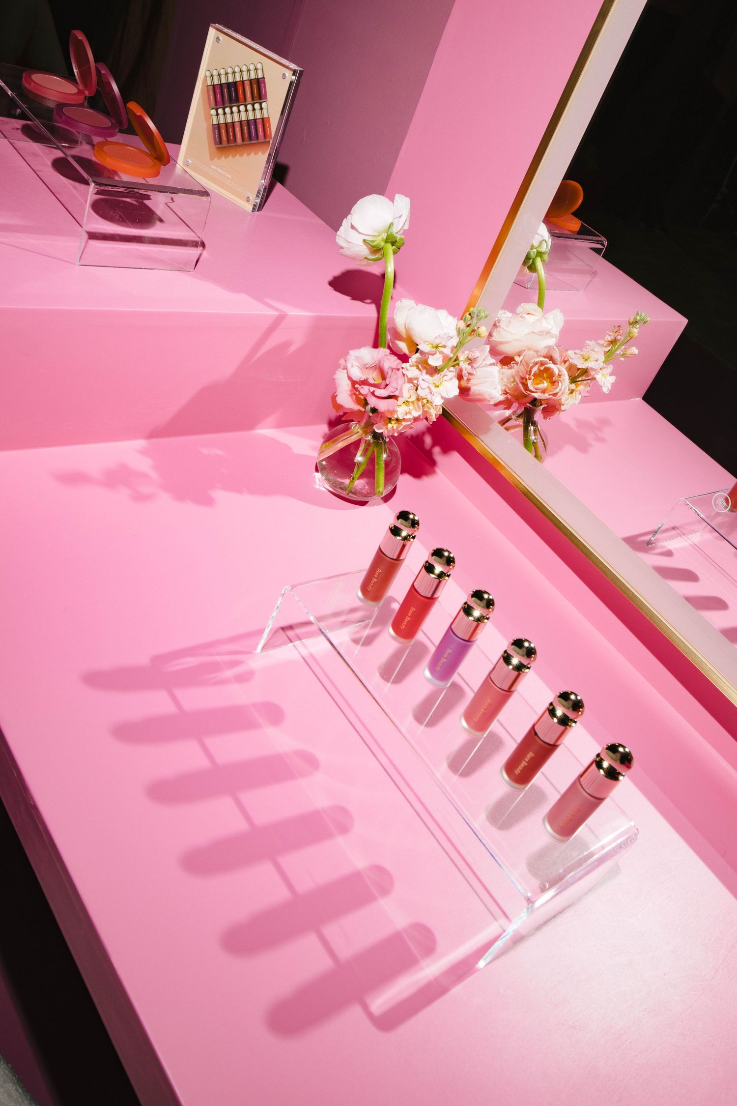 Cosmetic products displayed on pink illuminated platforms creating dramatic shadows.