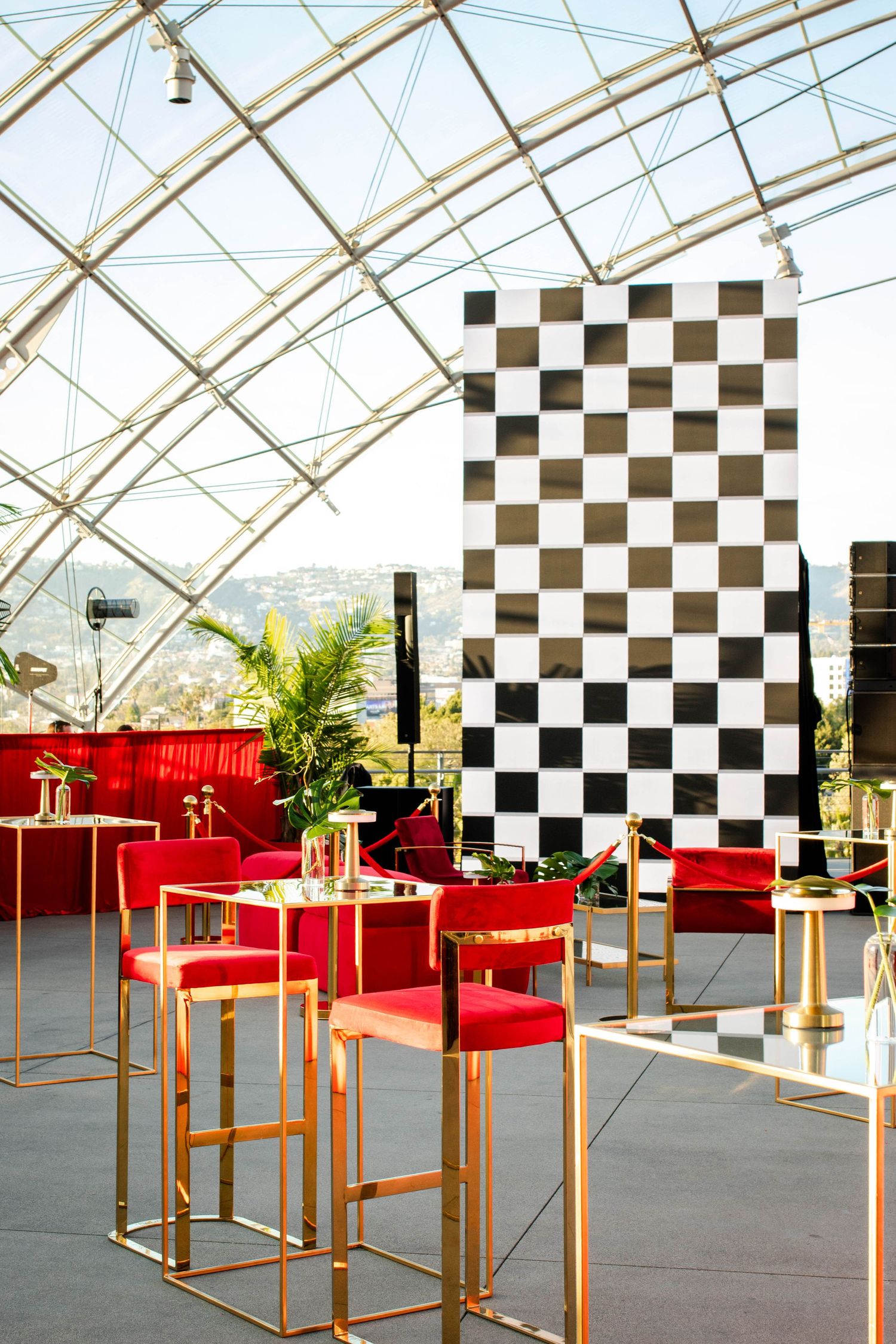 Exhibition space with checkered wall panels and red furniture displays under glass ceiling architecture.
