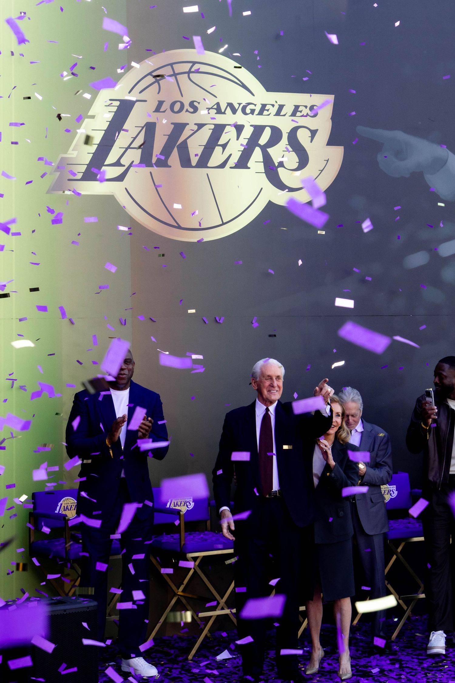 Confetti falls on stage at a Los Angeles Lakers event featuring the team logo backdrop with guests seated in director chairs.