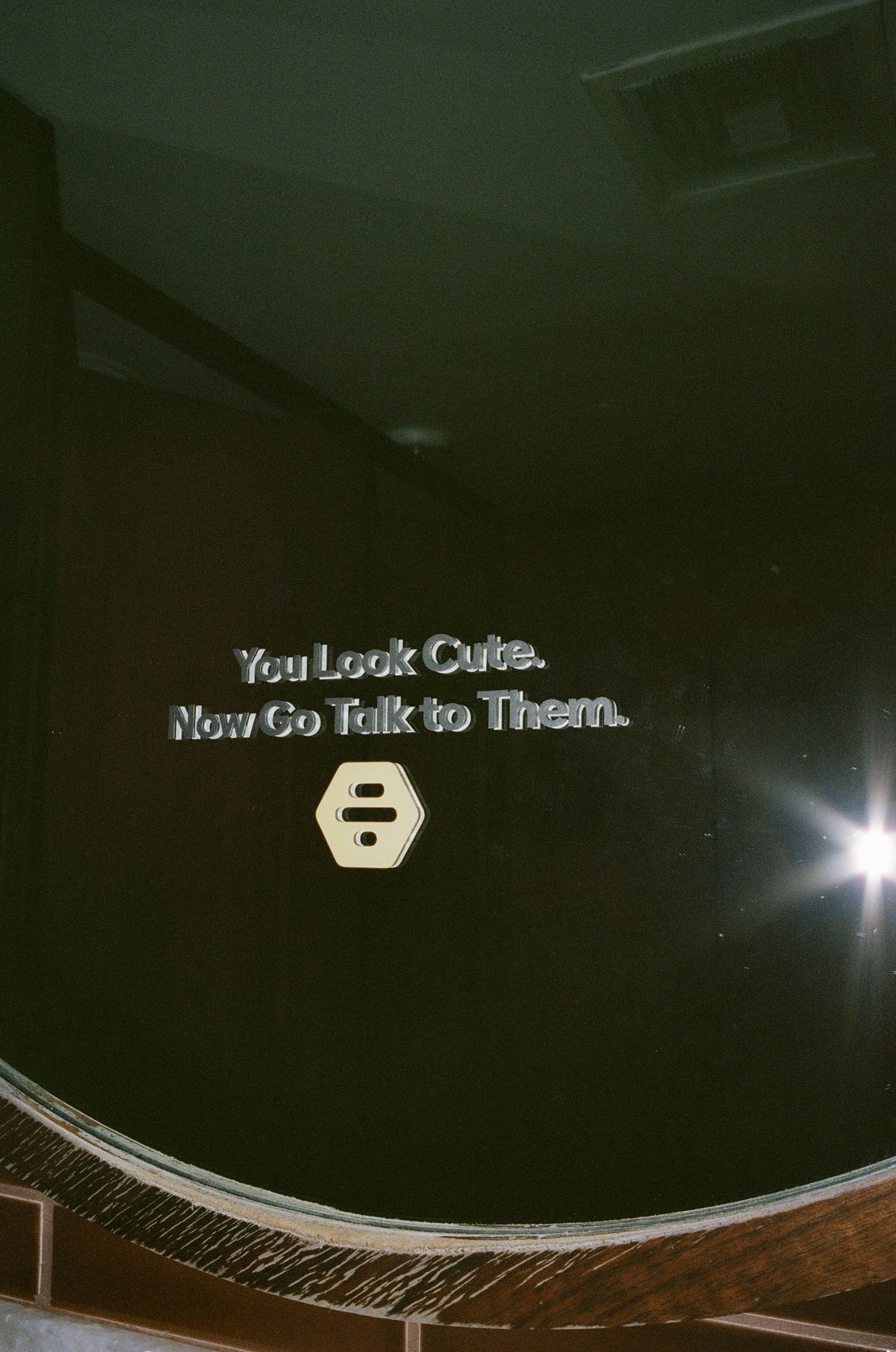 Motivational sign reading 'You Look Cute. Now Go Talk to Them.' with a hexagon logo on a dark wall.