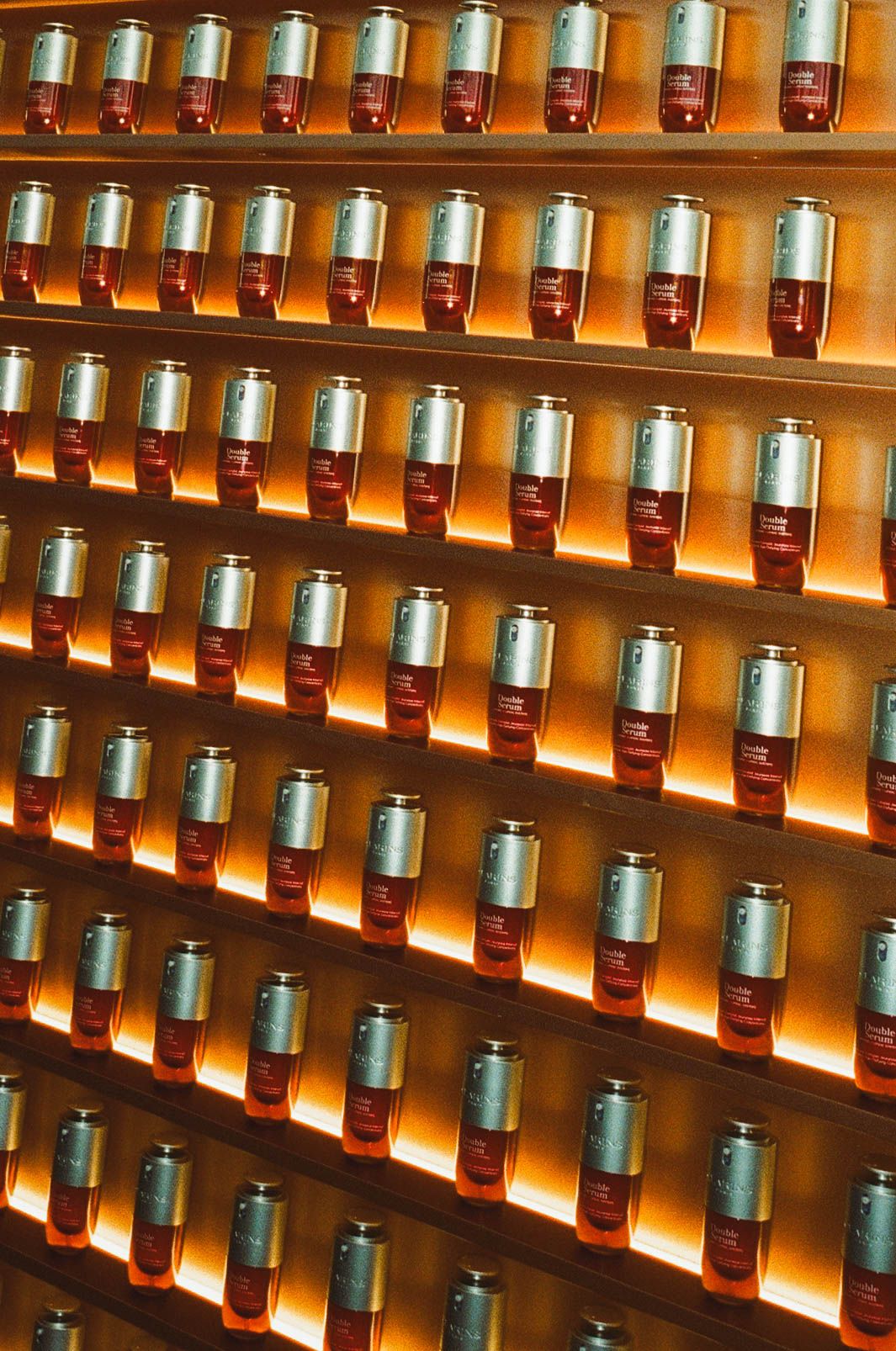 Rows of amber glass bottles with silver caps displayed on illuminated wooden shelves in a luxury retail store.