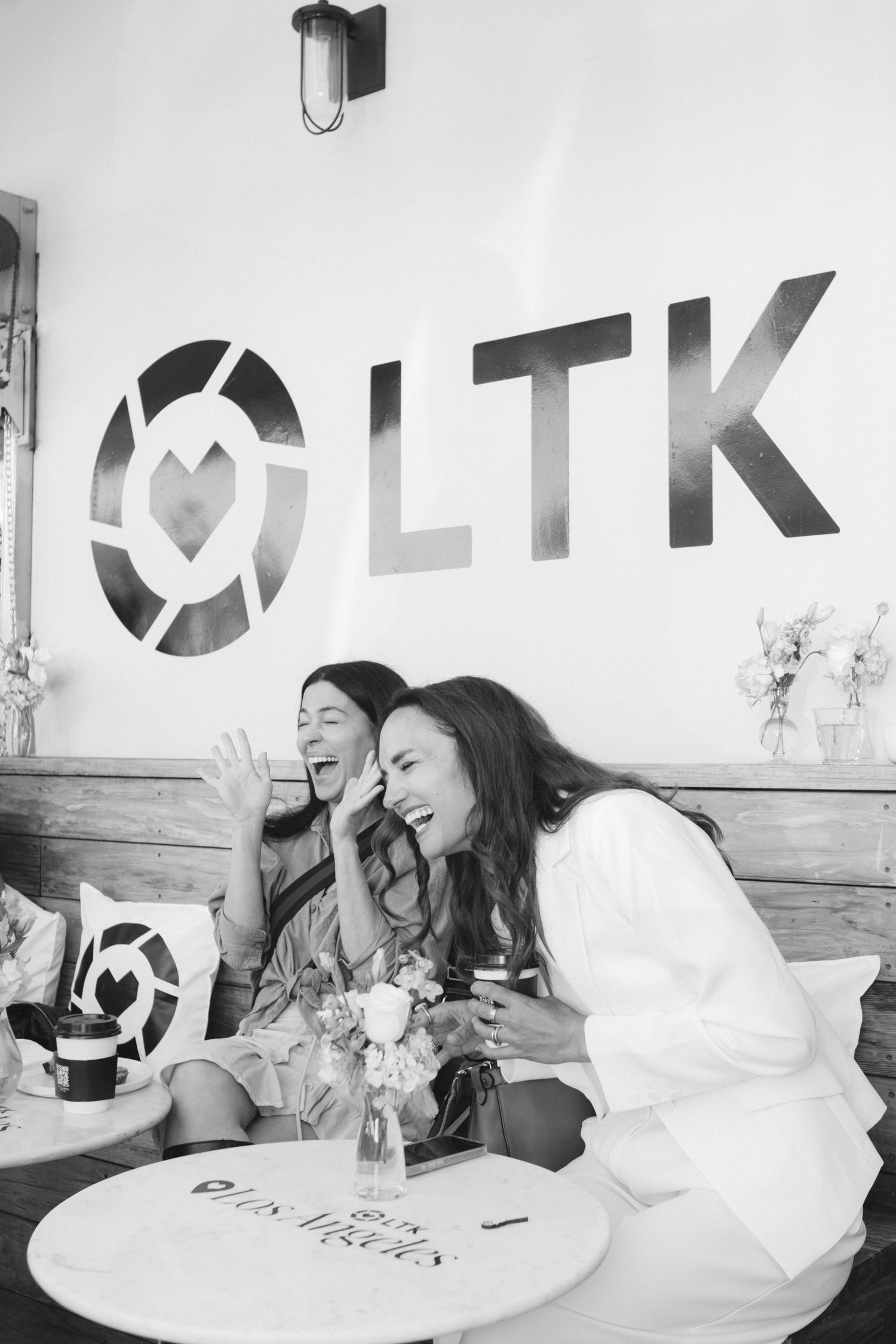 Black and white photo of LTK branded wall with people laughing at cafe table.