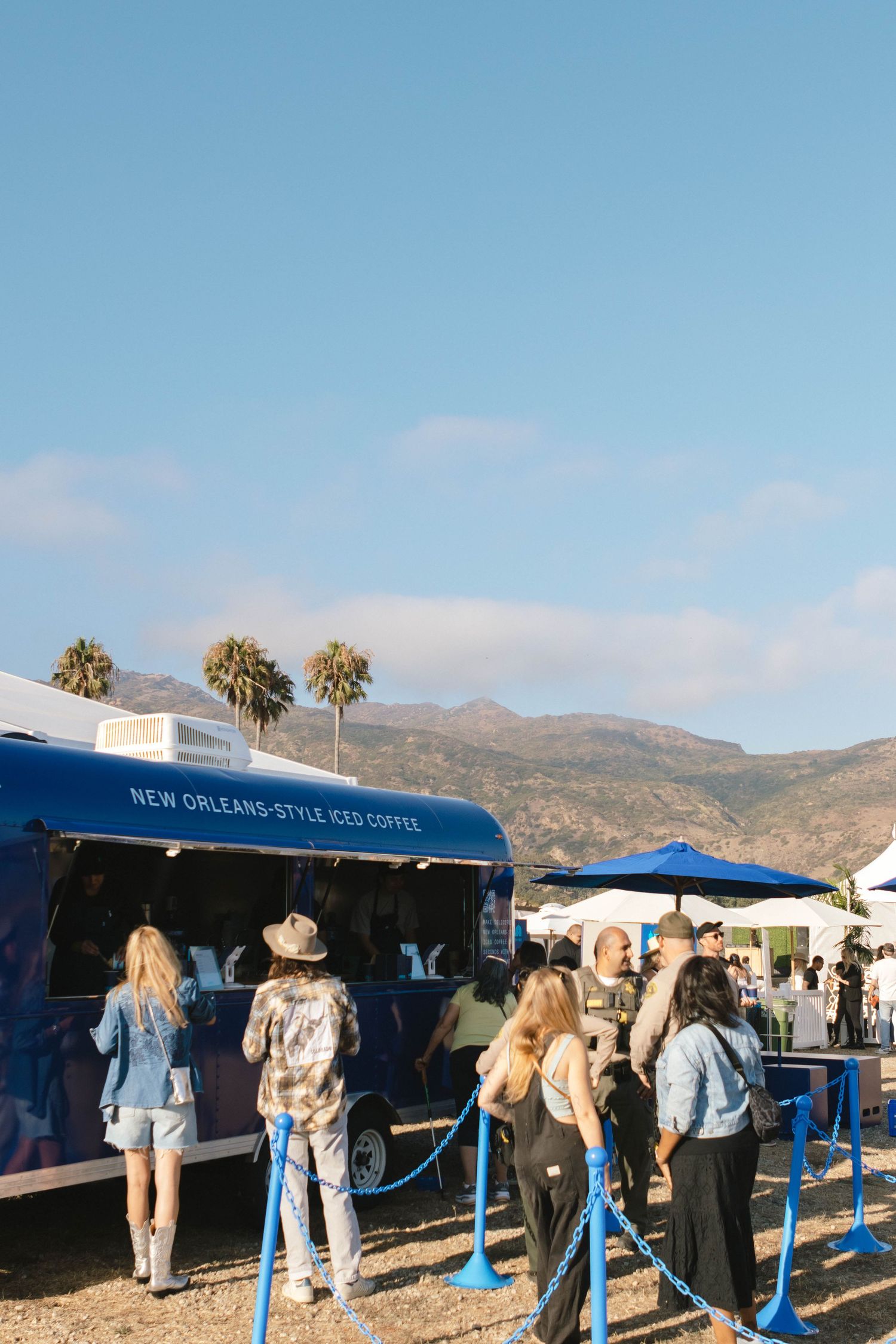 People waiting in line at blue coffee kiosks with mountains in the background.