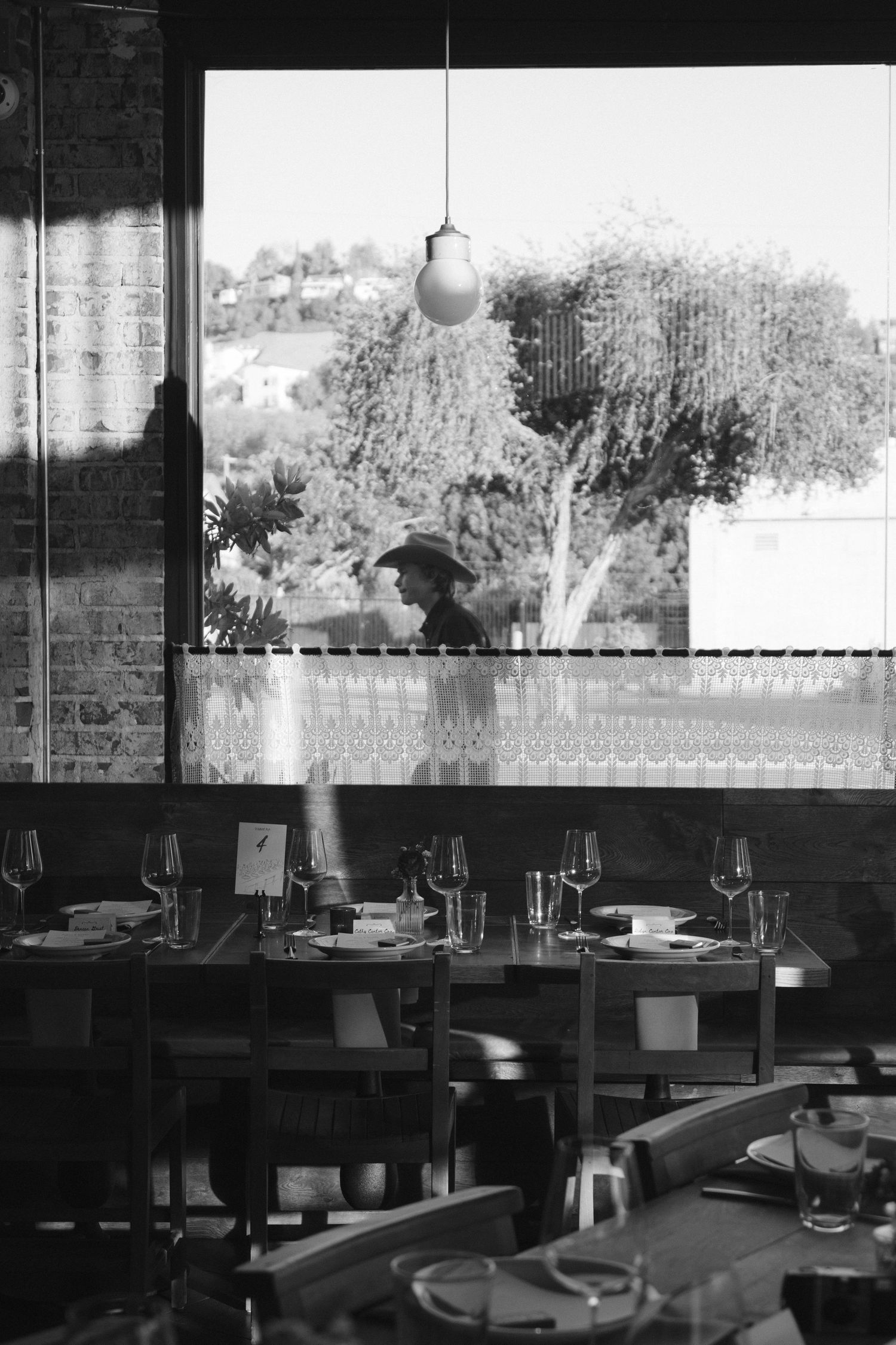 Black and white interior of an upscale restaurant with large windows overlooking a garden setting.