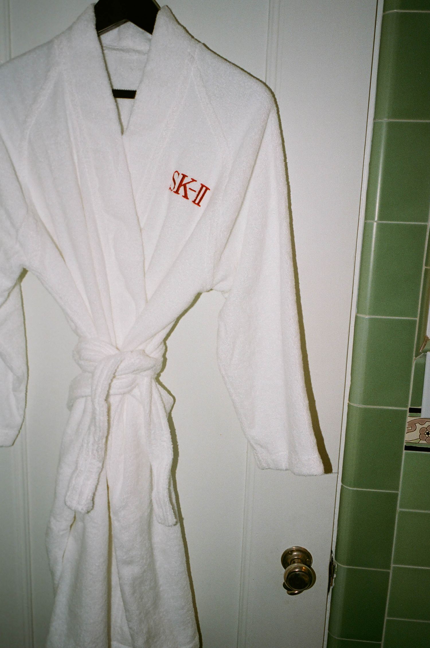 White bathrobe with red SK-II logo embroidery hanging on door.