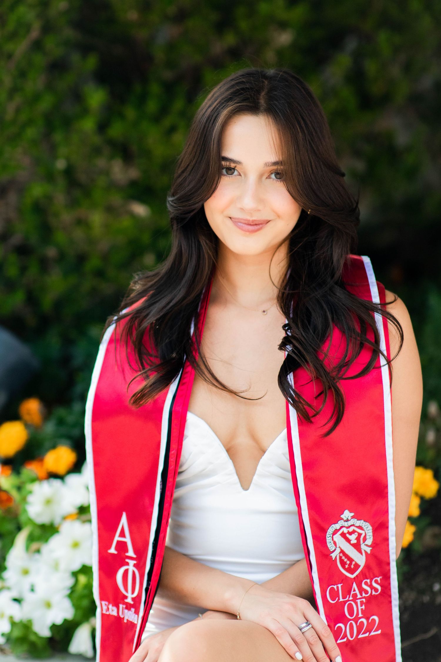 Graduate in white dress wearing red graduation stole with Class of 2022 emblem.