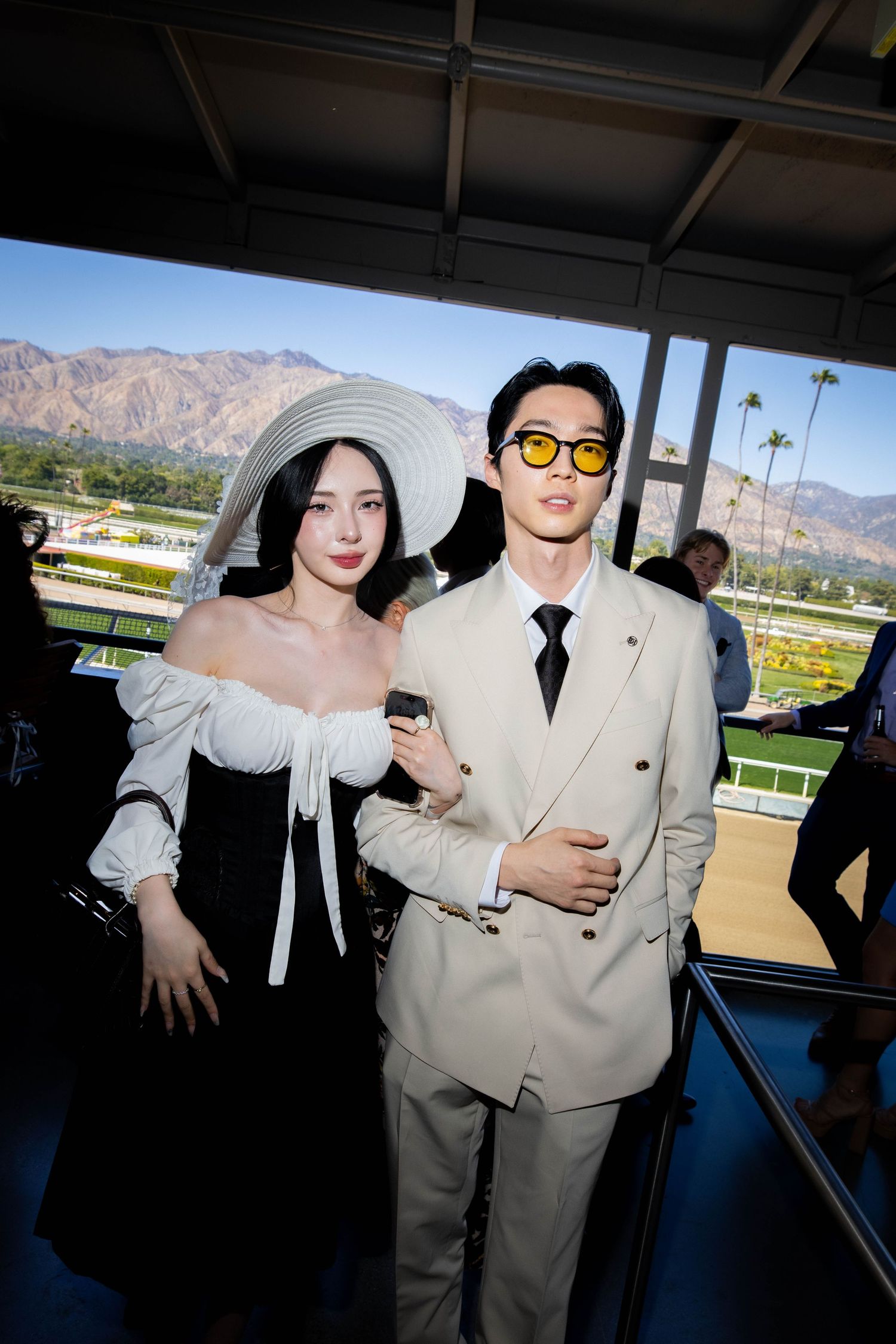 A couple poses together at a formal event, with the woman wearing white and the man in a light colored suit.