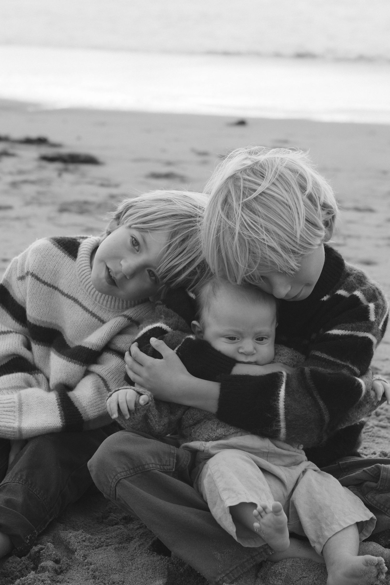 A black and white photo series shows a small child laying down and cuddling with a large dog on a beach.