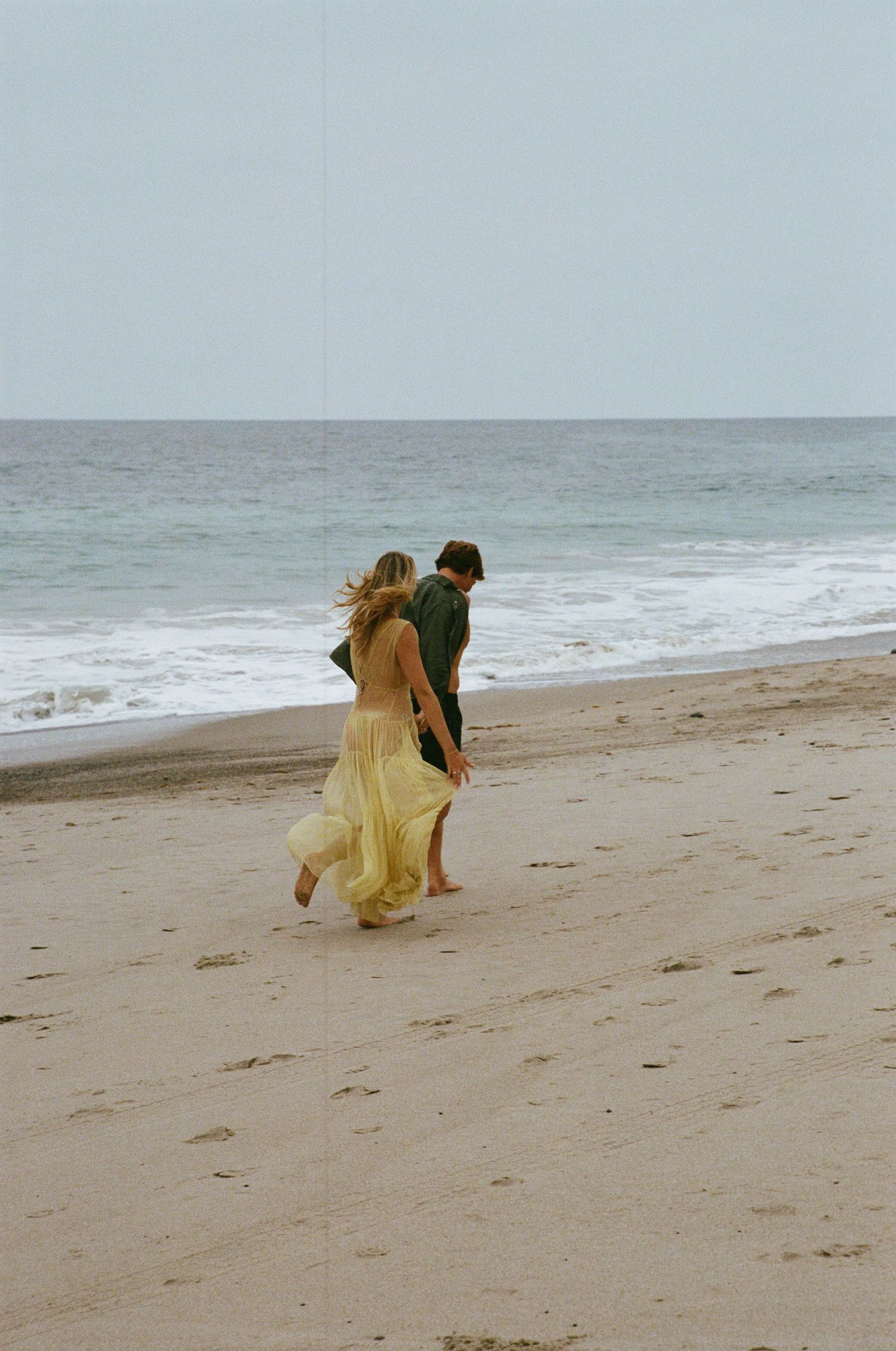 A person in a yellow dress runs joyfully along a misty beach shoreline.