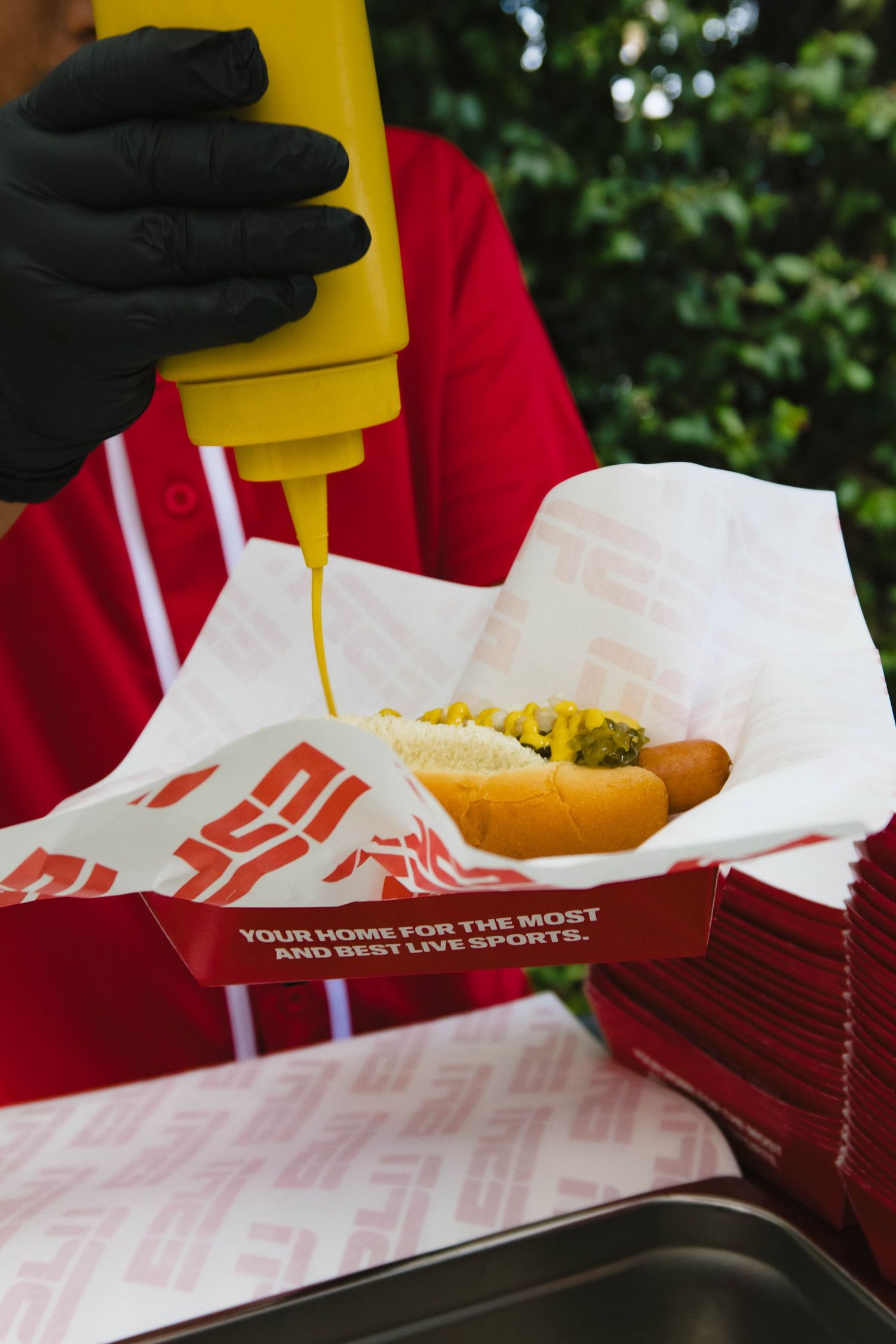 Hot dog being served in branded paper wrapper at outdoor sports event.