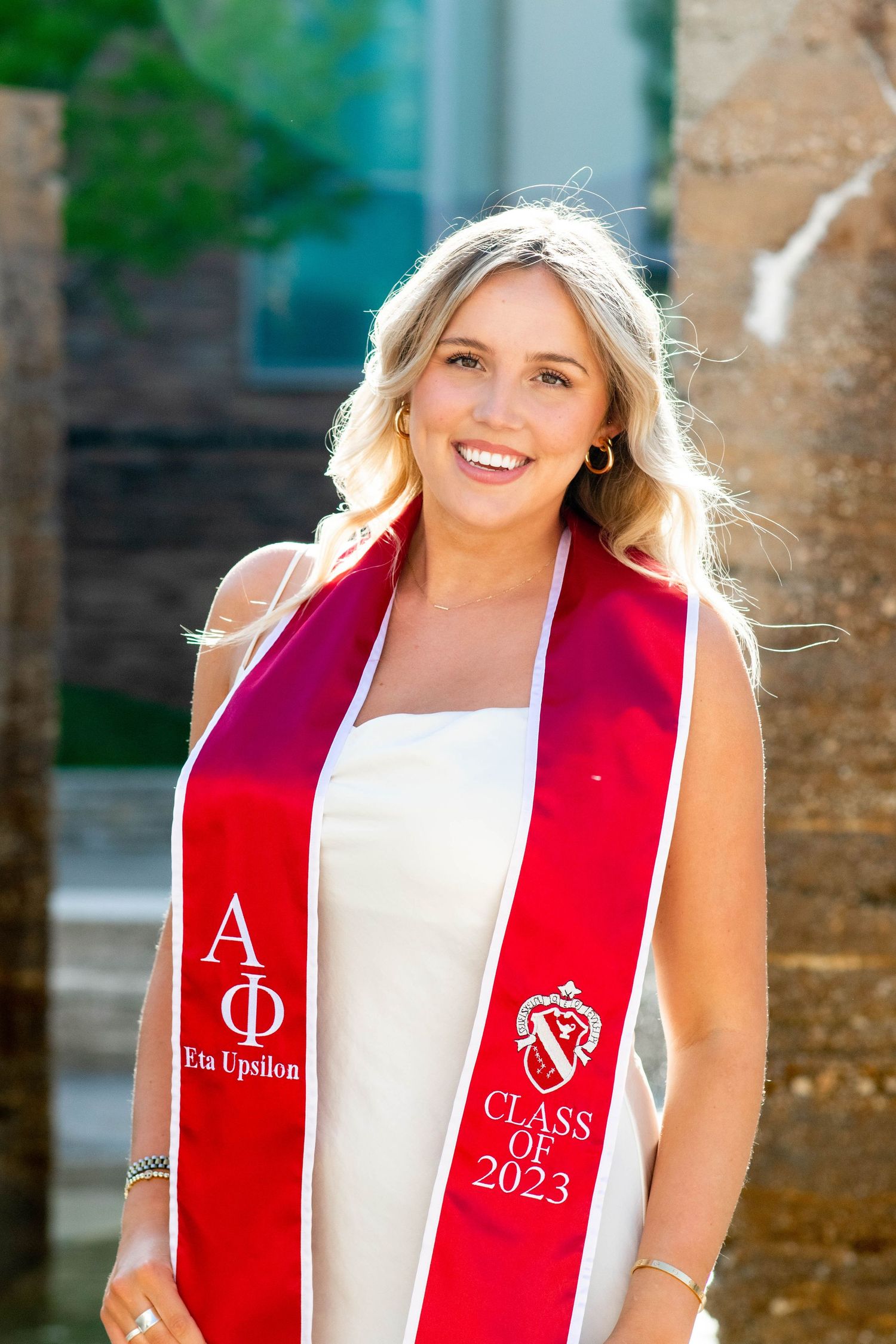 Graduate wearing red and white graduation stole with Class of 2023 emblem in outdoor portrait session.