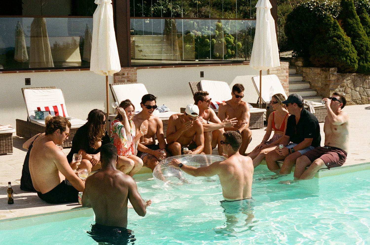 People enjoying a pool party with multiple participants swimming and socializing in a bright blue swimming pool.