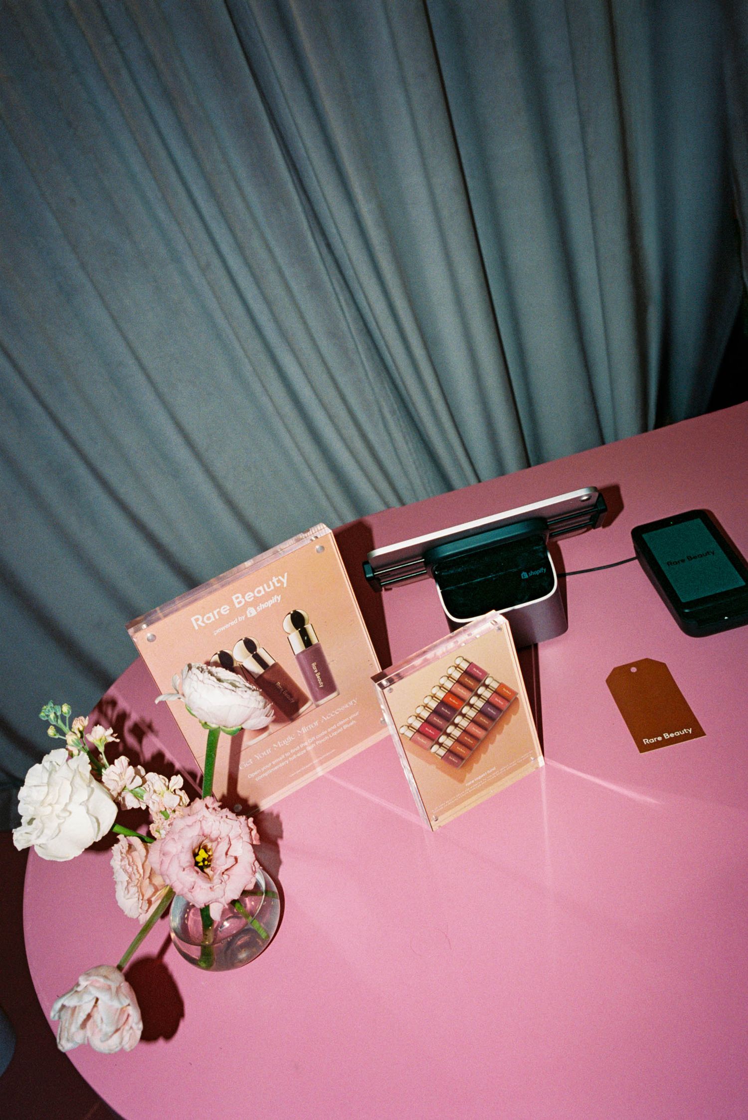 Beauty products and makeup displayed on a pink surface with decorative flowers.