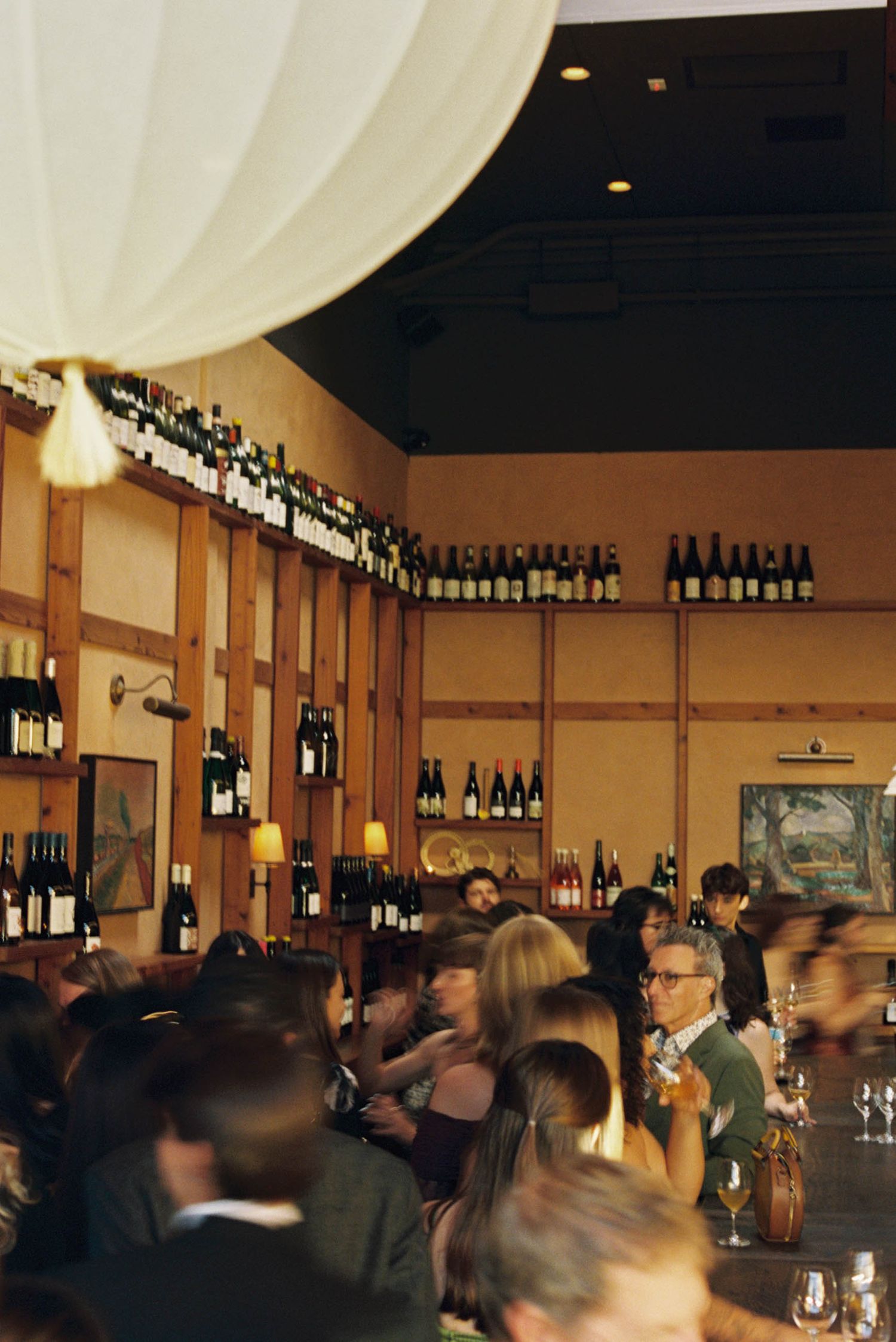 Busy wine bar interior with bottles displayed on shelves and mingling guests.