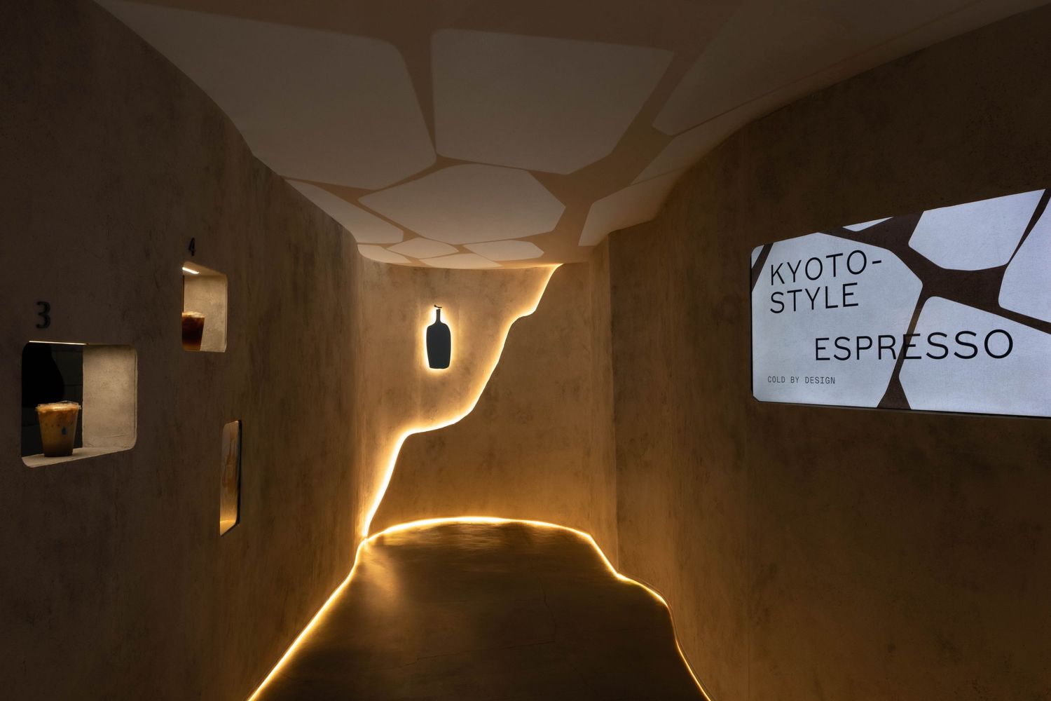 Kyoto-style espresso bar interior with warm LED lighting, textured cave-like walls, and minimalist Japanese design aesthetic.