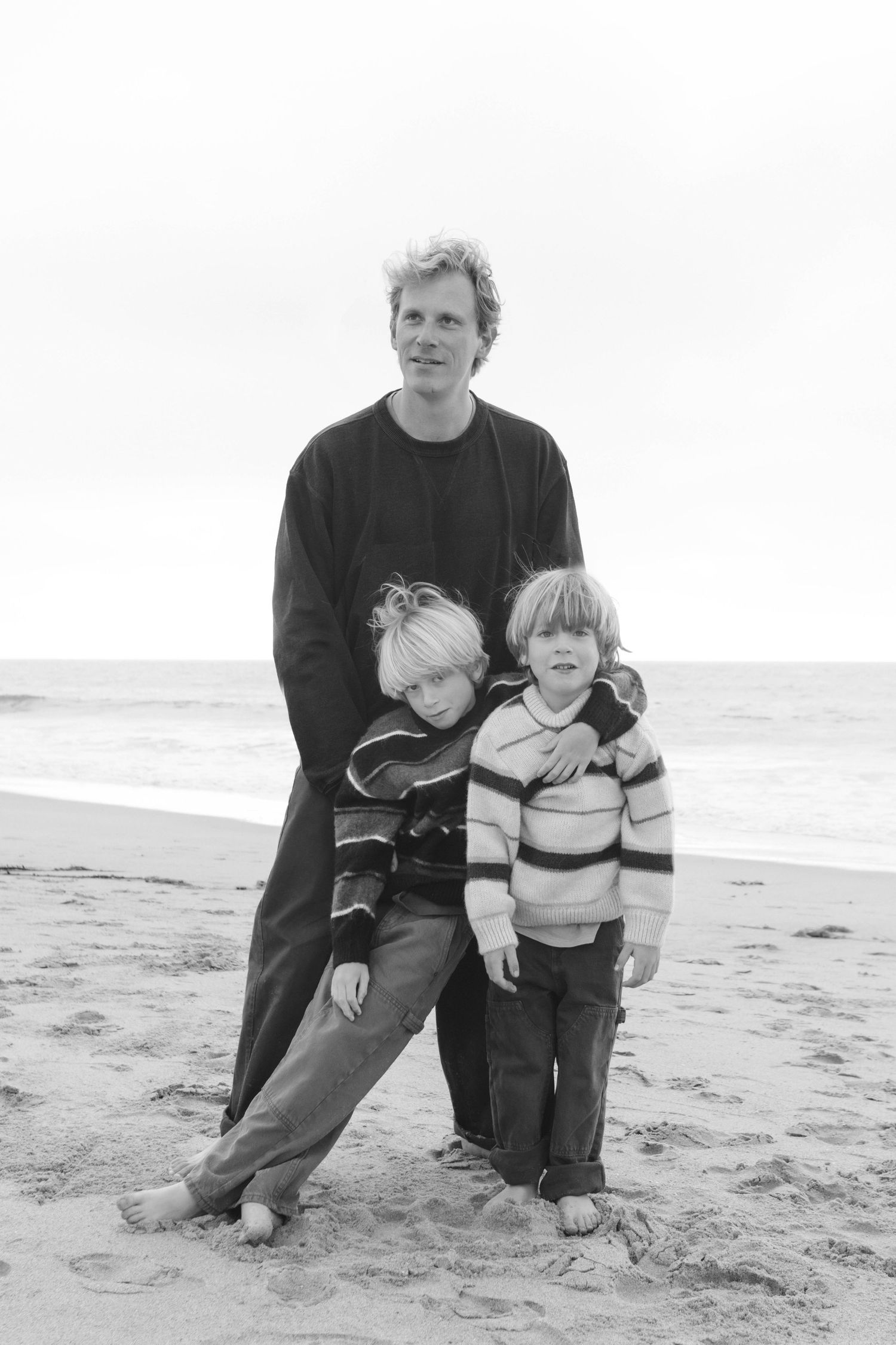 Family sitting together on sandy beach in black and white photograph.