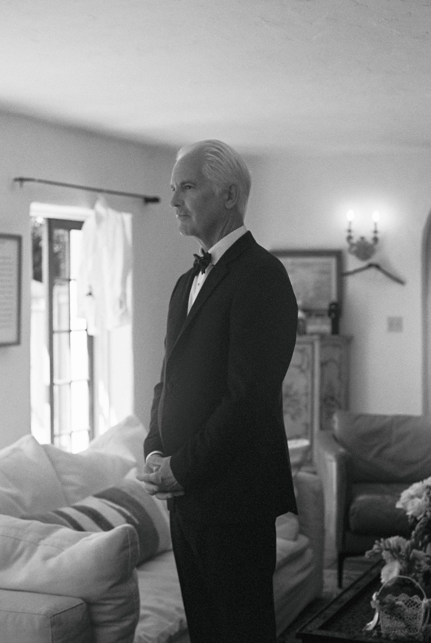 Black and white photo of someone in formal attire standing in a sunlit room.