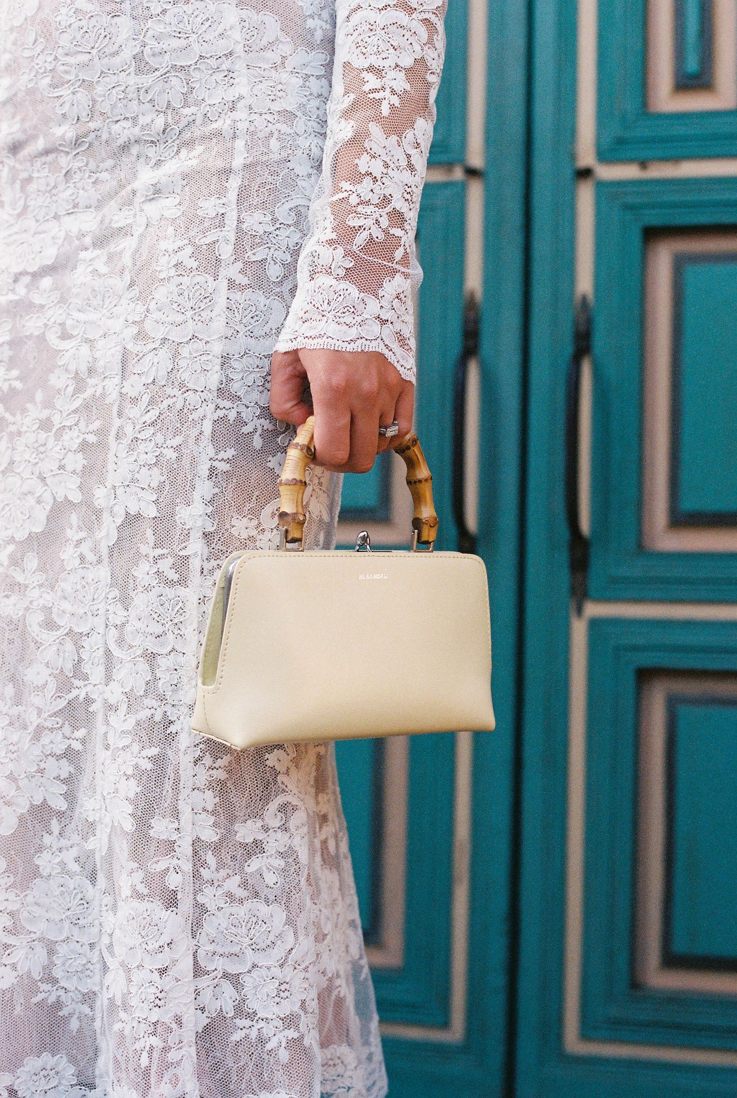 White lace wedding dress detail with a cream clutch purse against turquoise doors.
