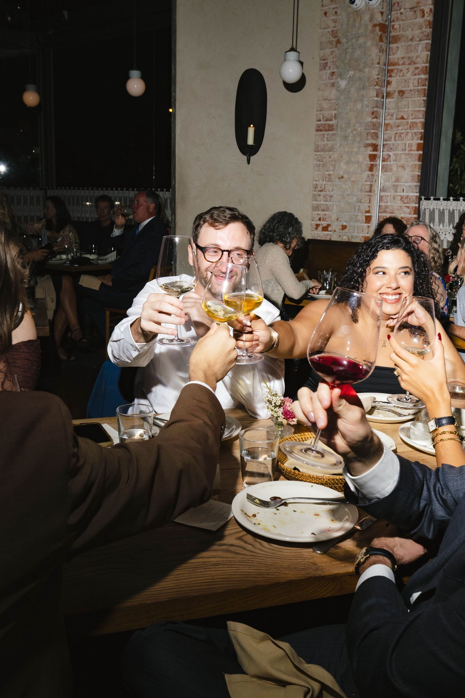 Wedding reception guests raising glasses for a toast at a dimly lit dinner table.