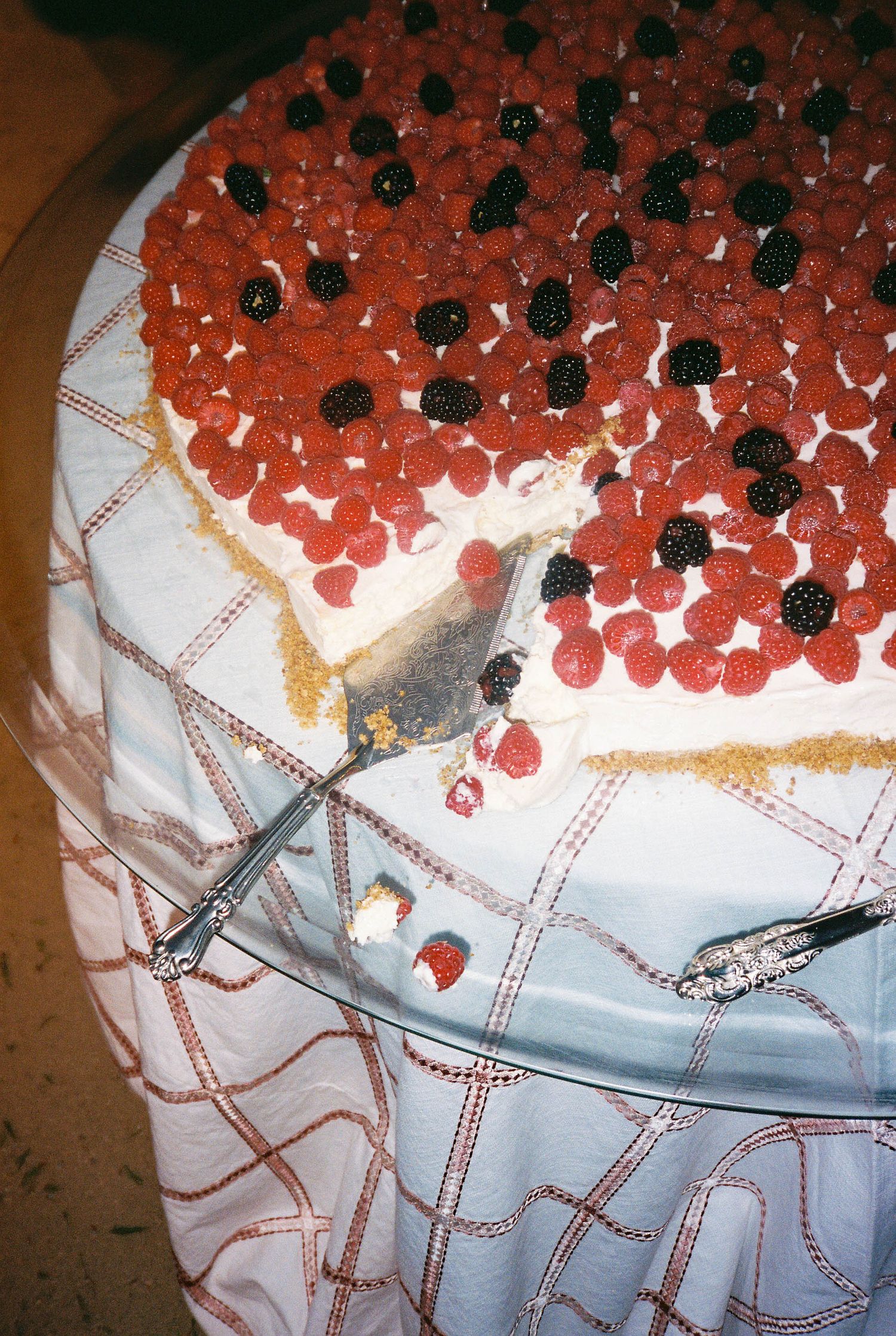 Wedding cake decorated with red berries and black details on white lace-patterned frosting.