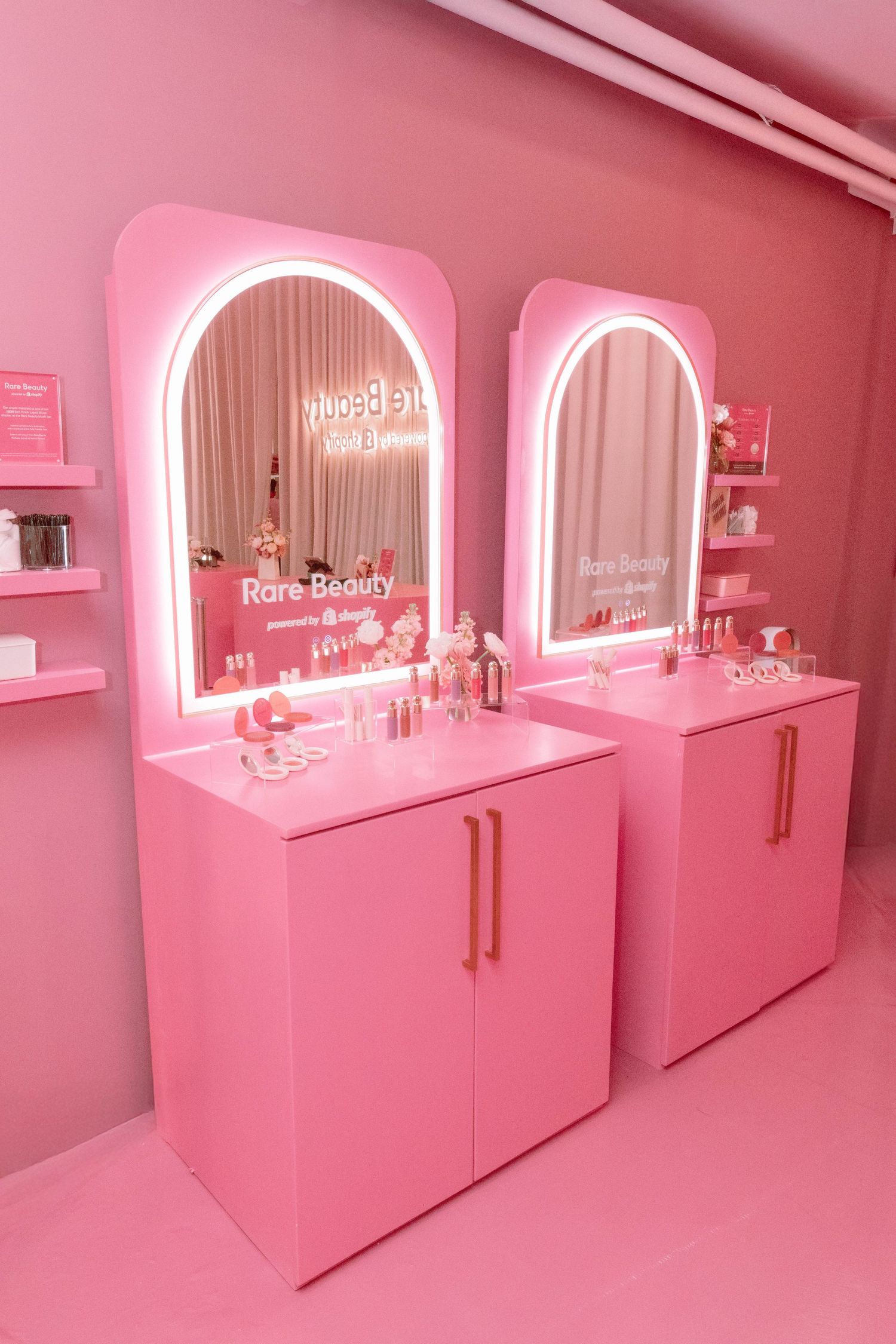 Modern pink beauty salon with illuminated vanity mirrors and sleek storage cabinets.