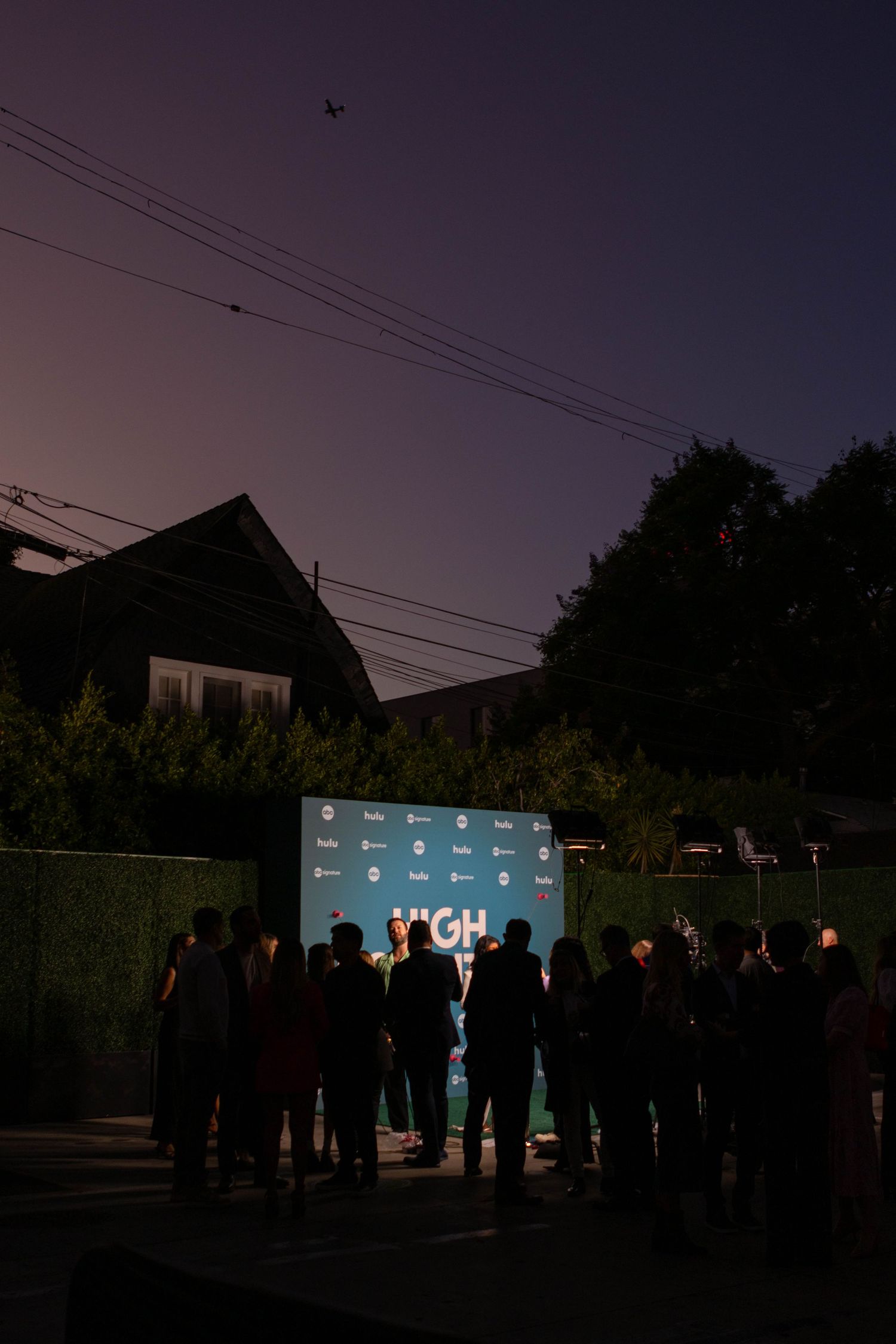 Silhouettes of people gathered around outdoor projection screen at dusk.