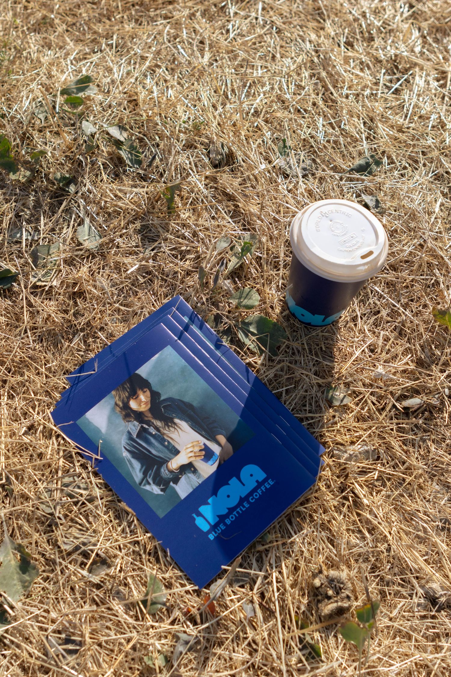 Coffee cups and branded materials displayed on dried grass or hay.