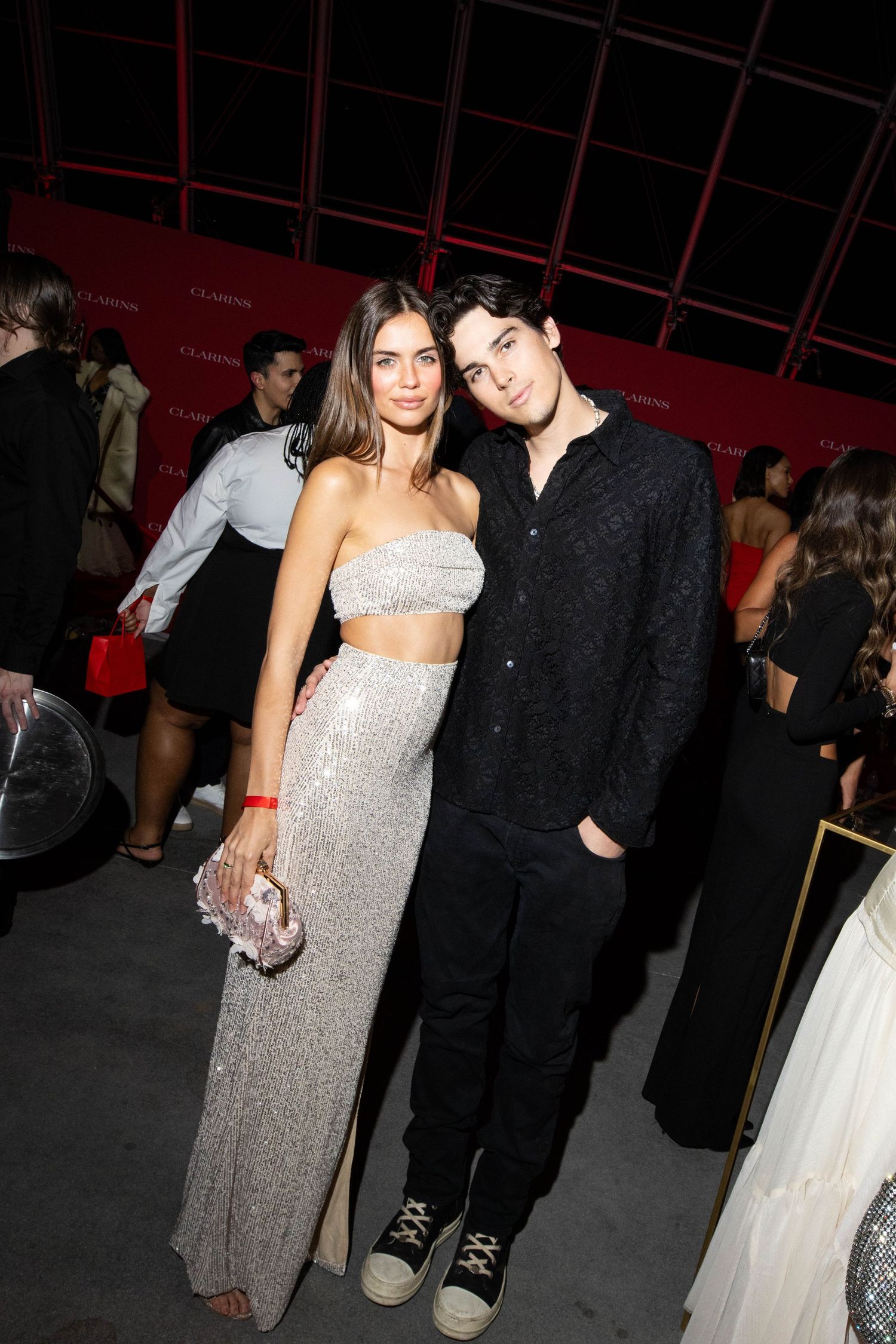 A couple poses together at a formal event, with one person wearing a sparkly silver gown and the other in dark attire.