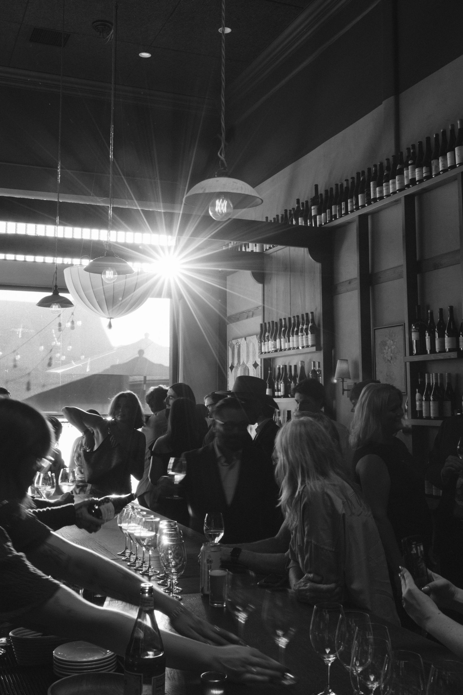 A dimly lit bar scene with patrons gathered at the counter and bright lights creating a moody atmosphere.