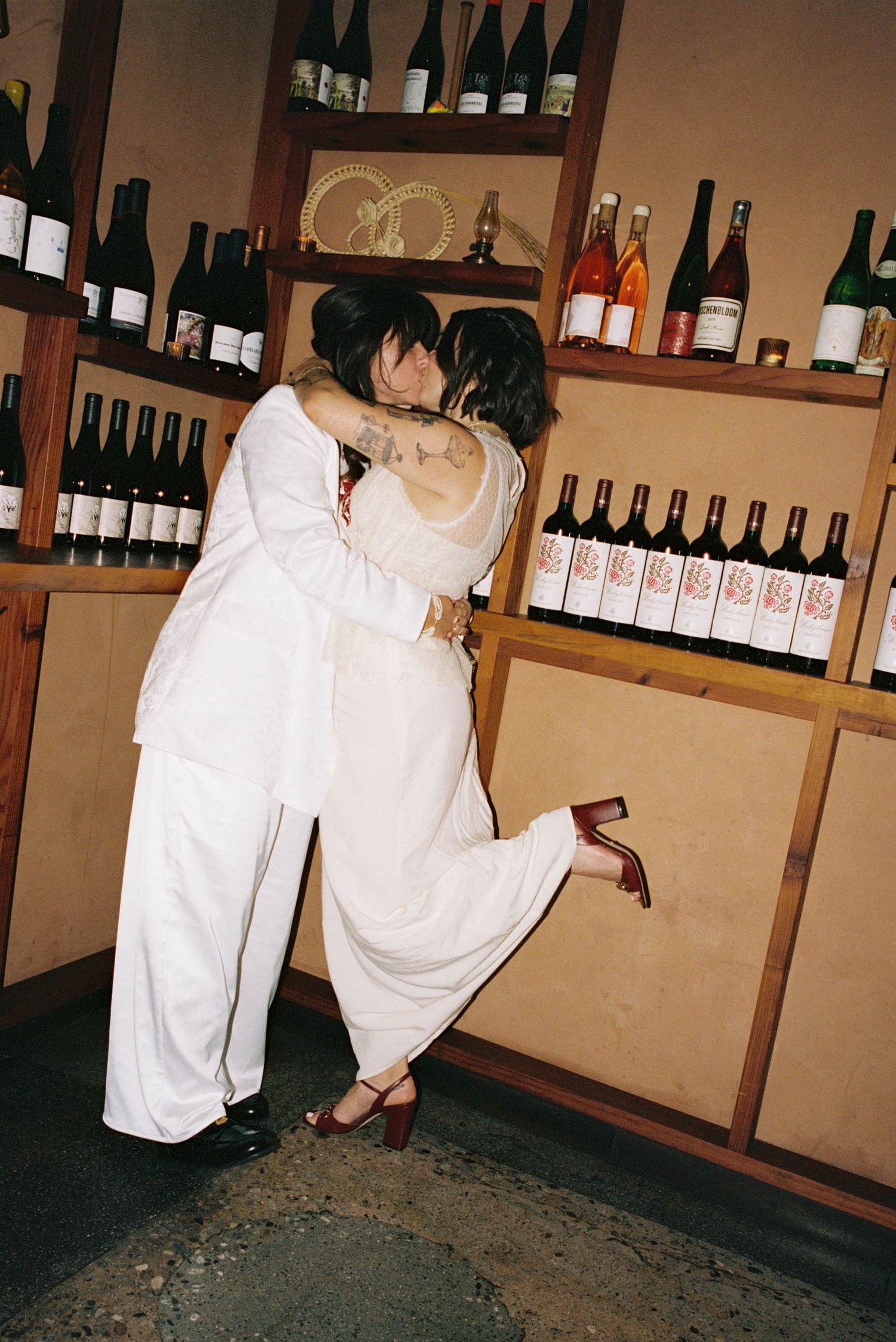 Two people in white clothing moving through a wine storage room.