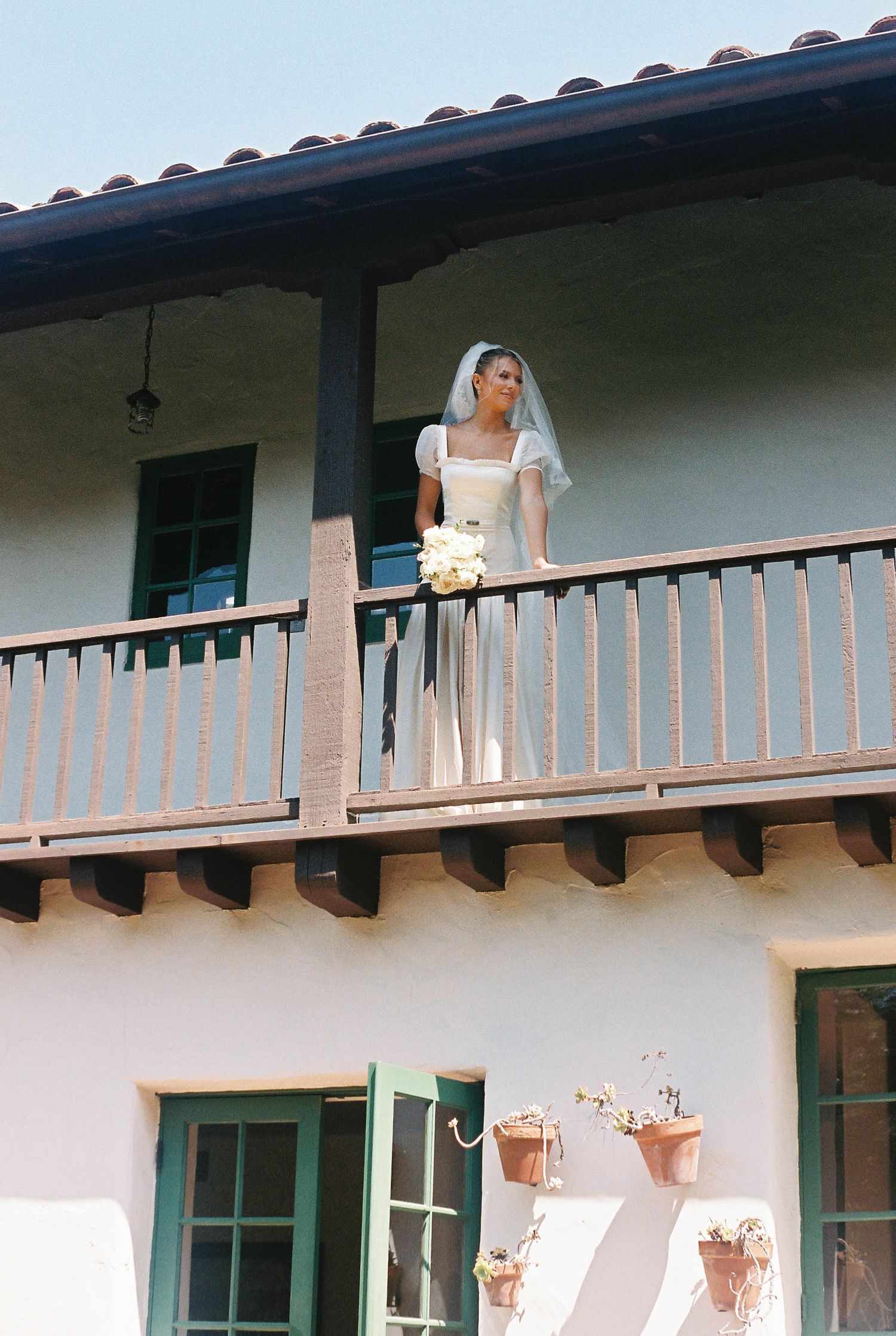 White Spanish-style building with a covered porch and wooden beams in bright sunlight.