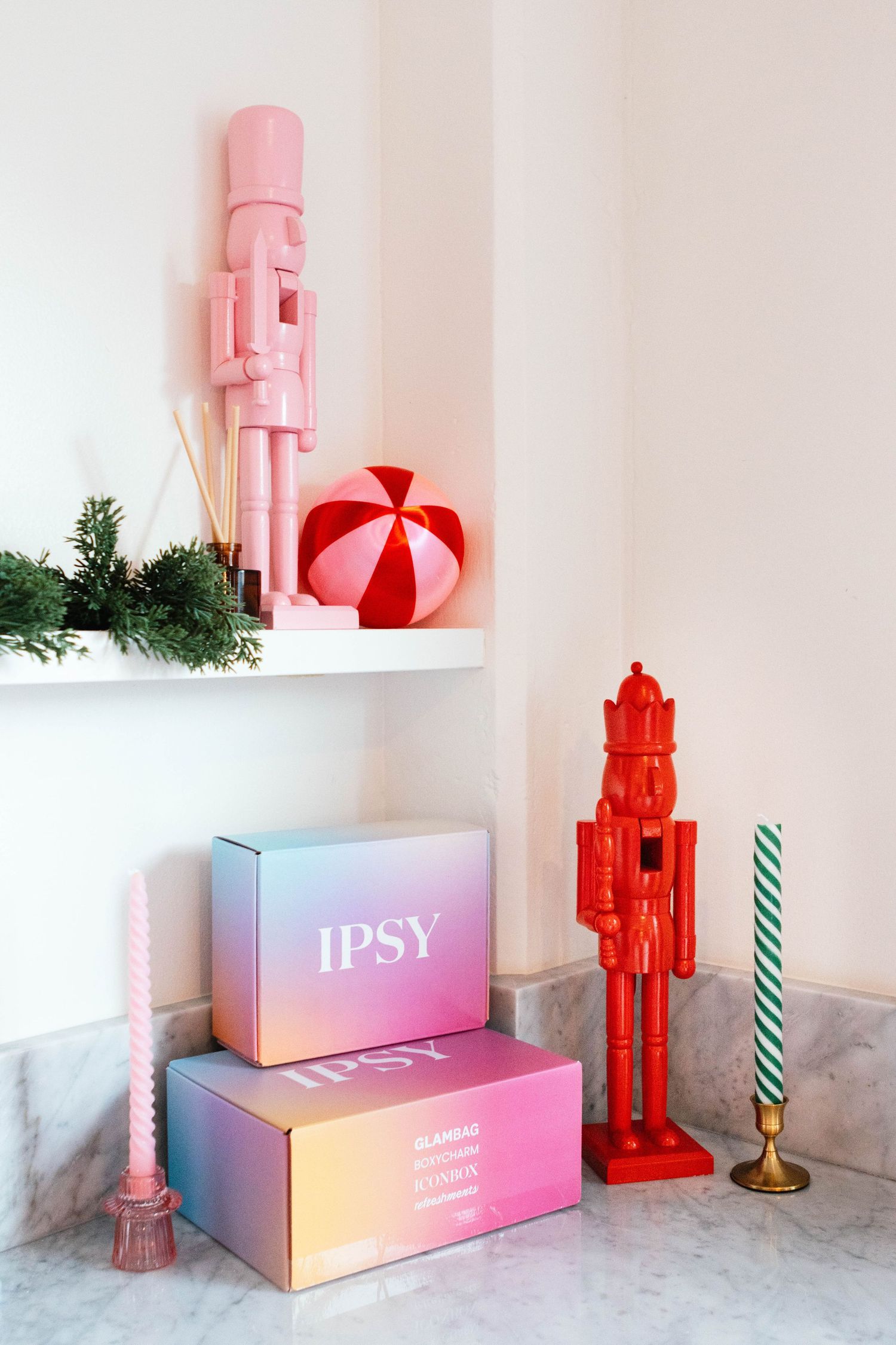 Pink and red nutcracker decorations displayed with Ipsy boxes on marble shelf.